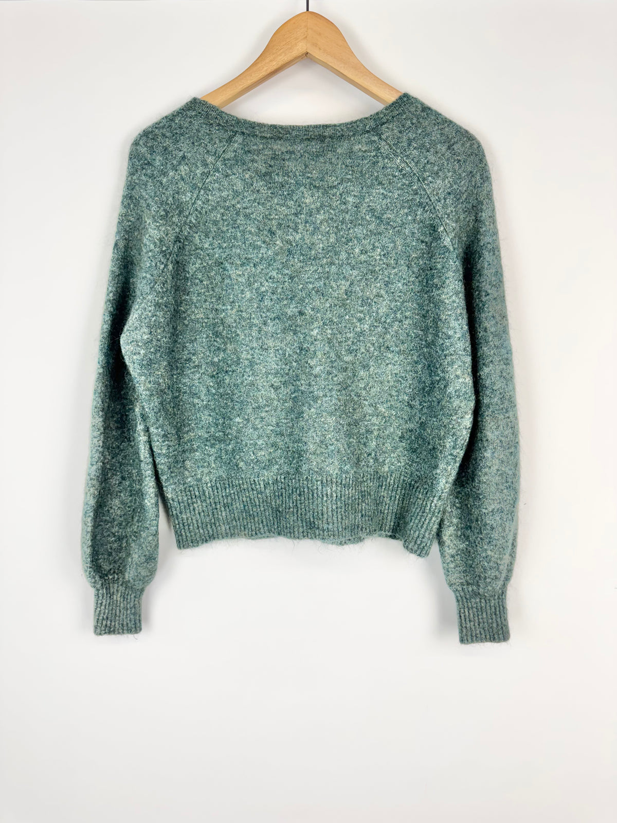Green sweater on a wooden hanger against a white background