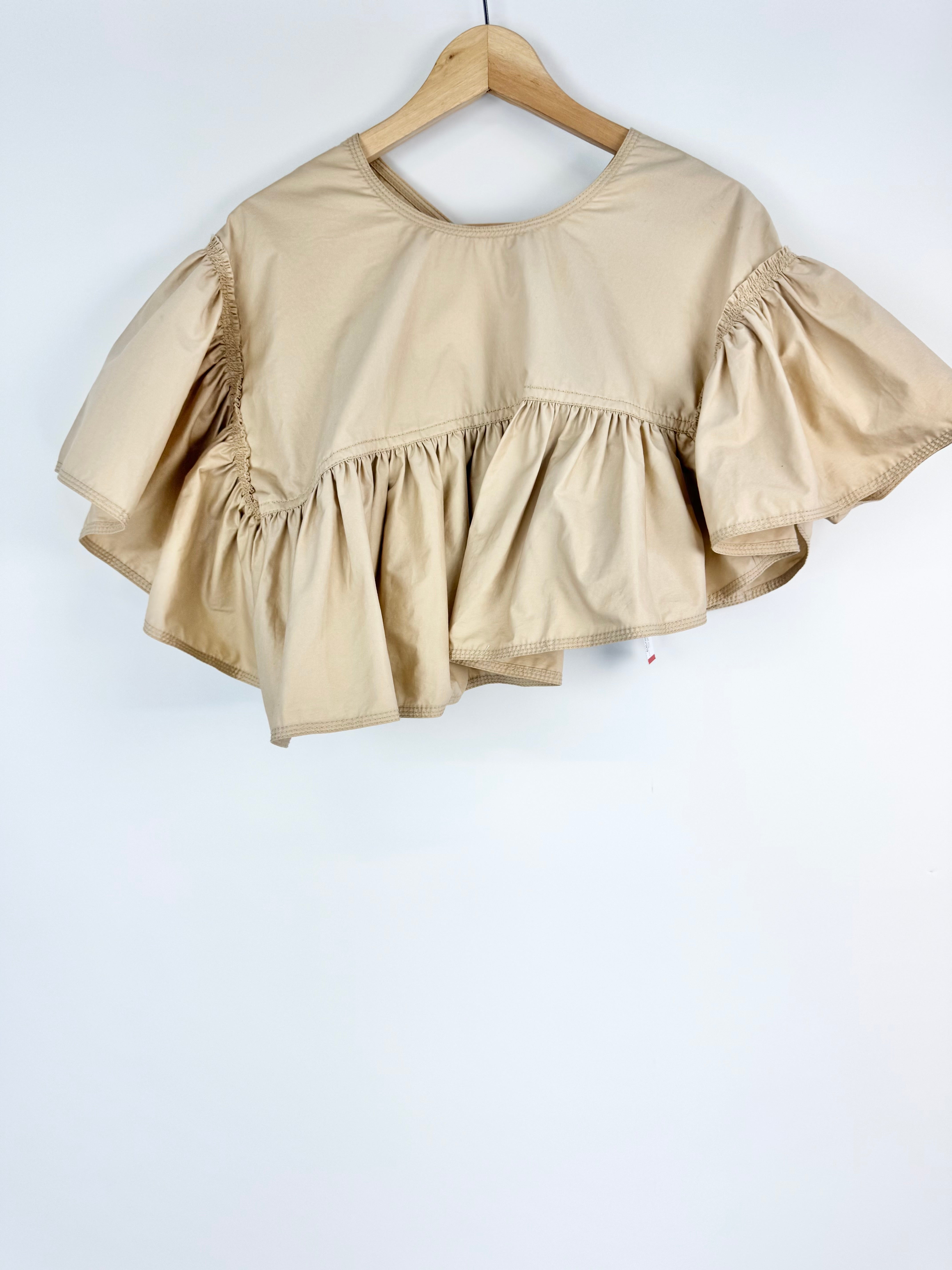 Beige blouse with ruffled layers on a wooden hanger against a white background