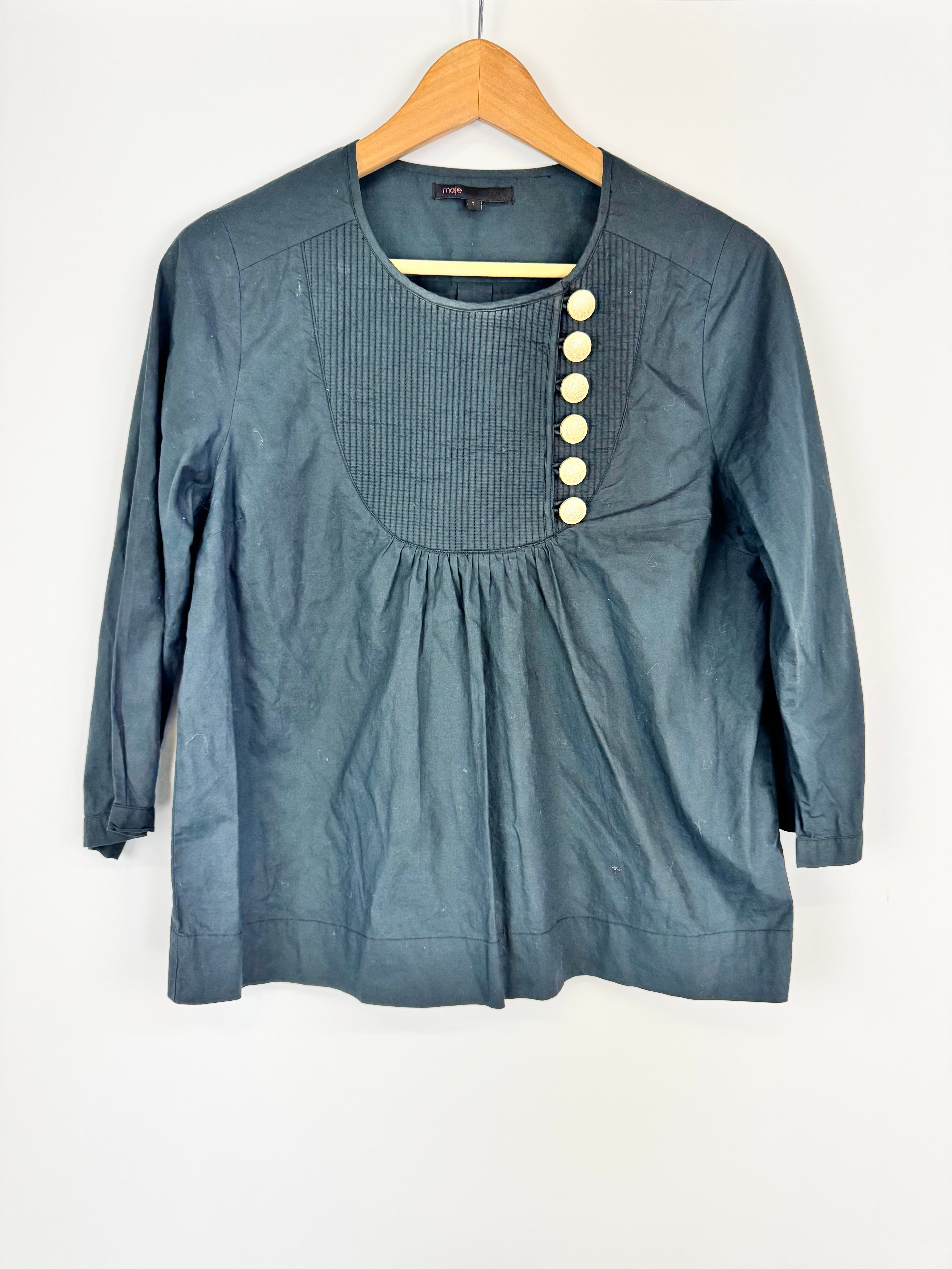 Blue blouse with gold buttons on a wooden hanger against a white background