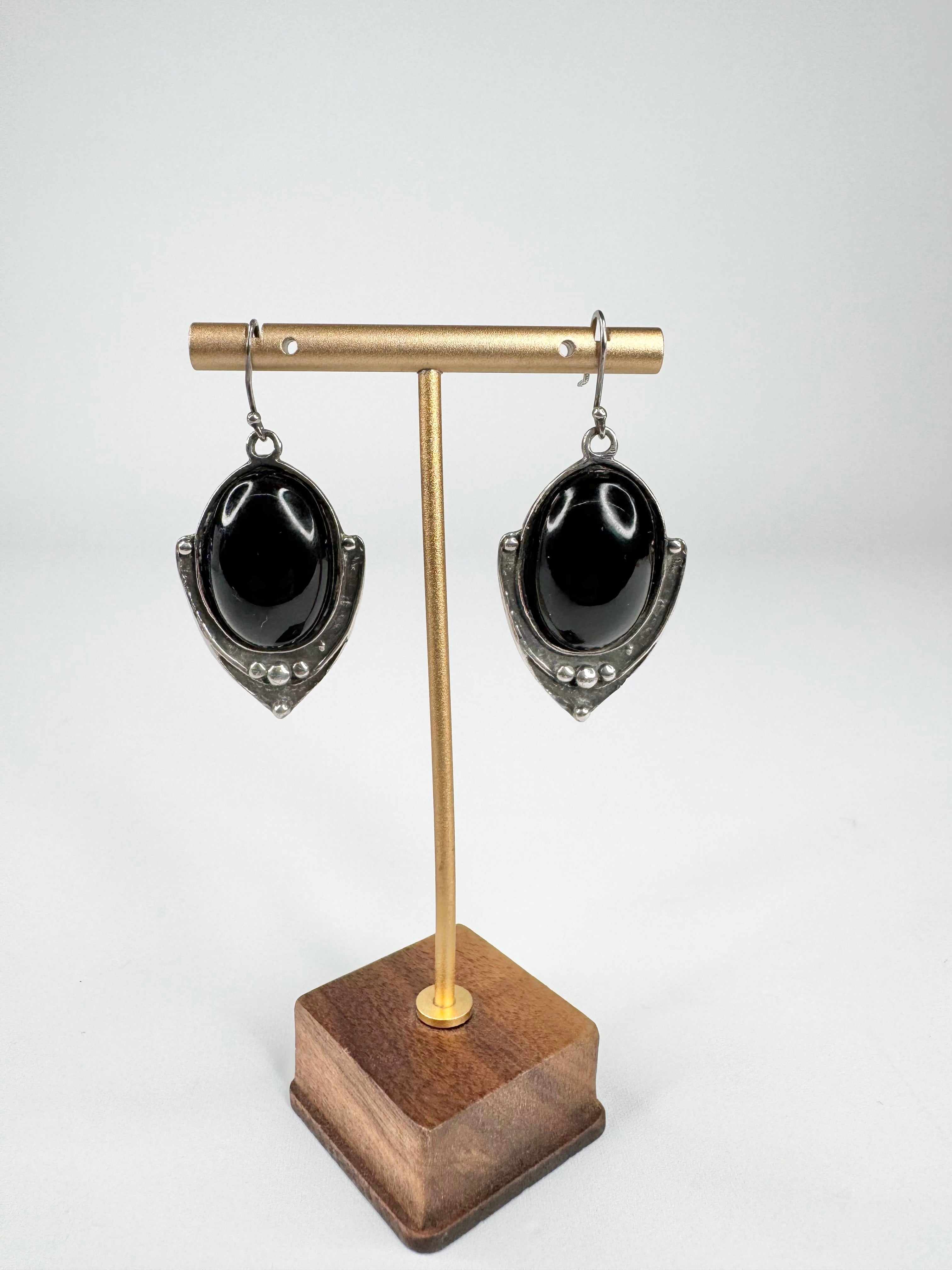 Pair of black teardrop earrings on a gold and wooden earring stand against a white background