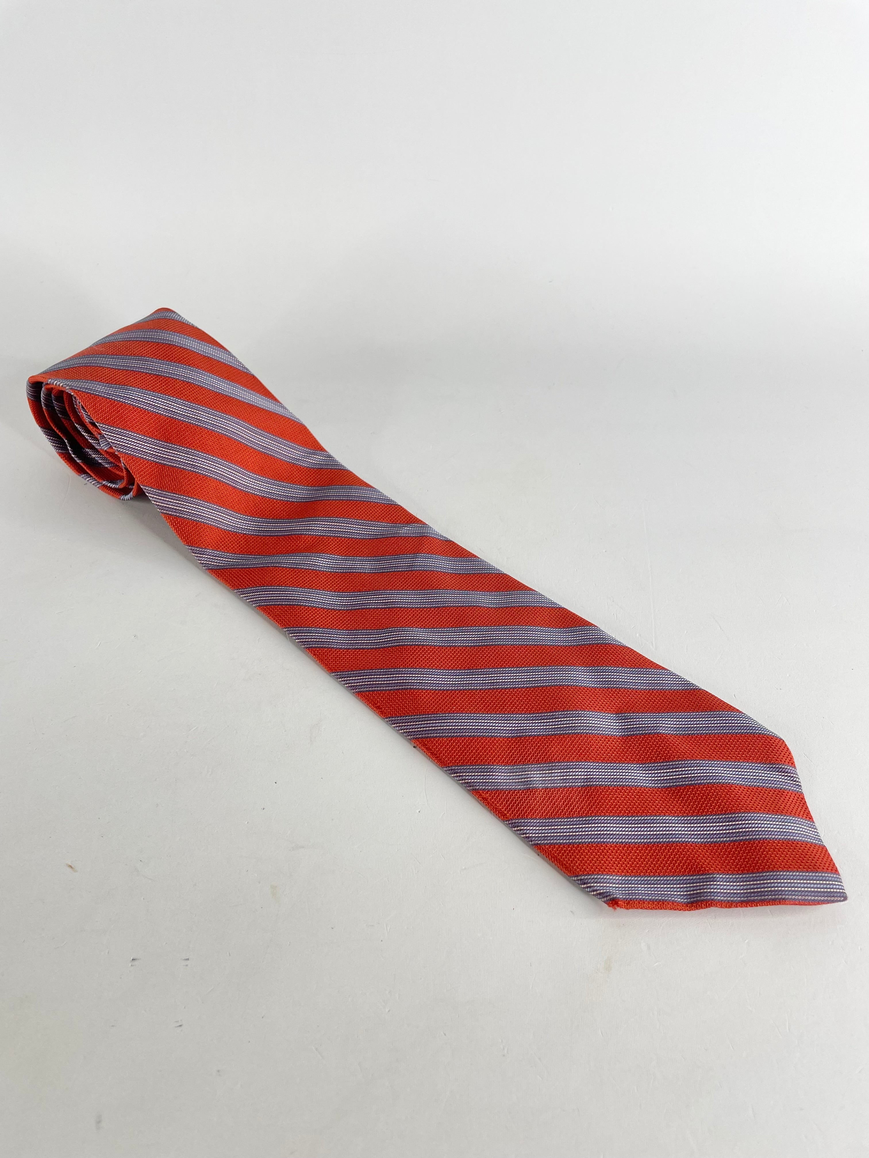 An orange and white striped silk tie laid out on a plain surface.