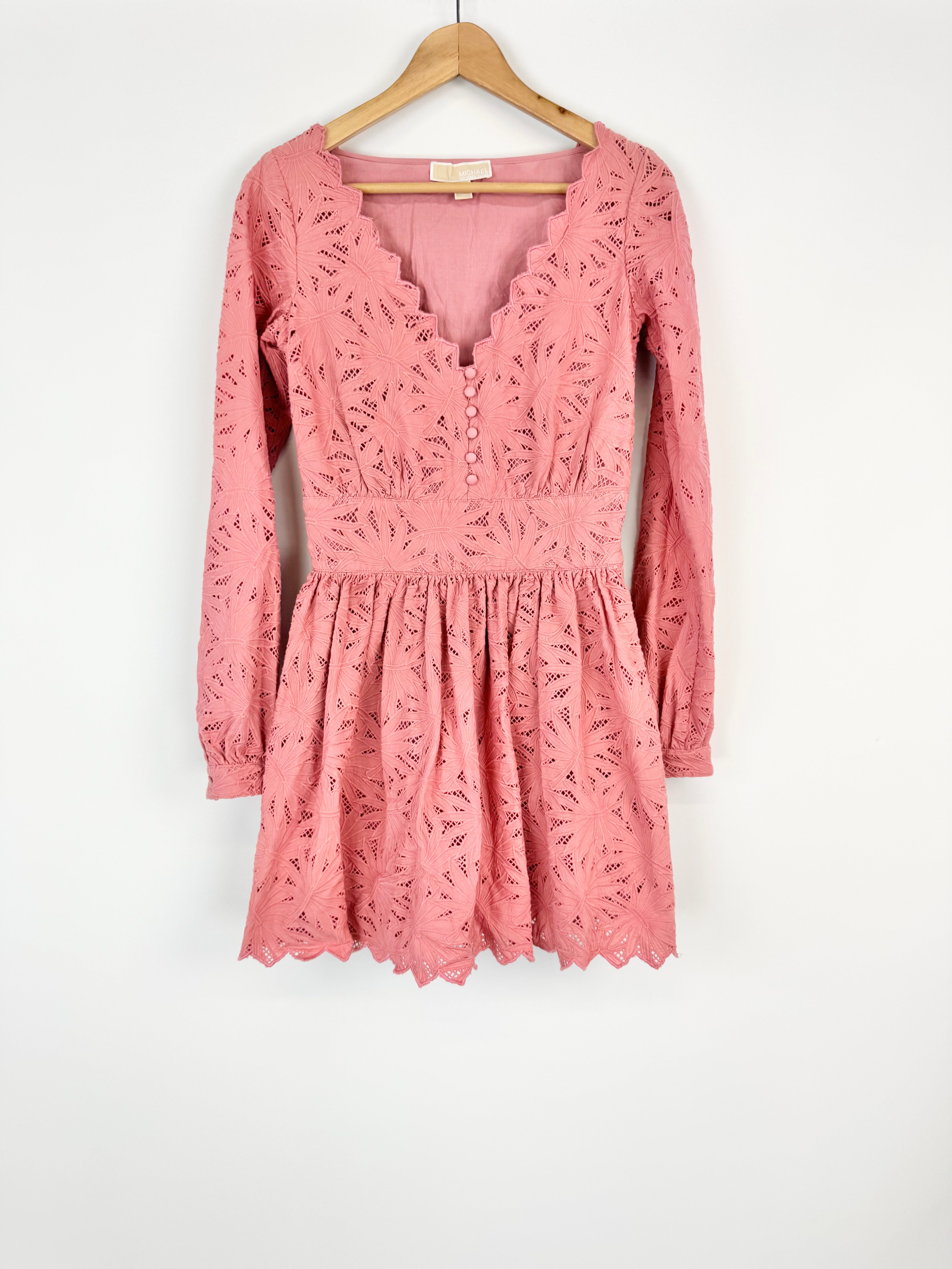 Pink lace dress on a hanger against a white background