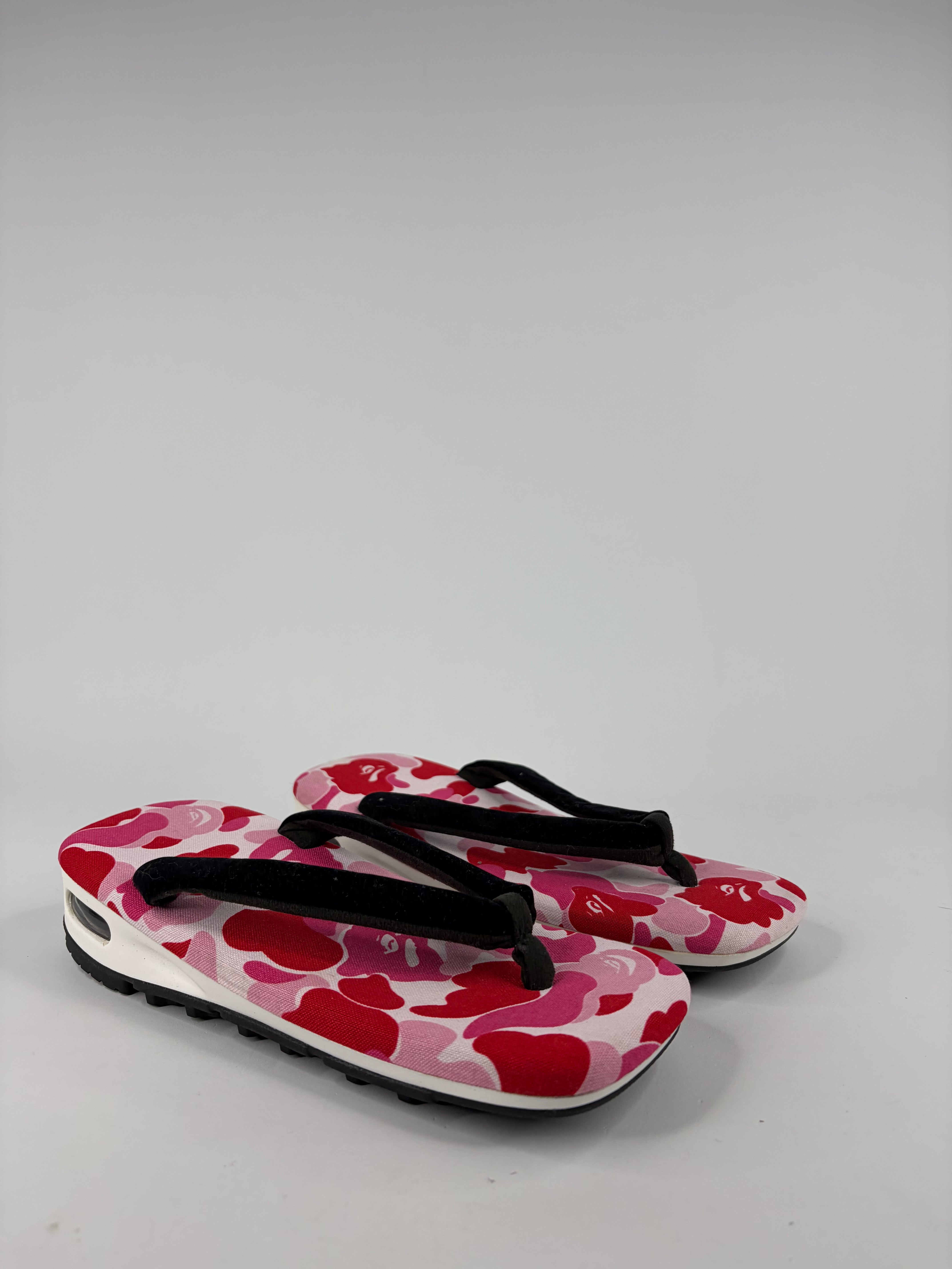 Pair of red and white floral-patterned sandals with a black strap on a gray background