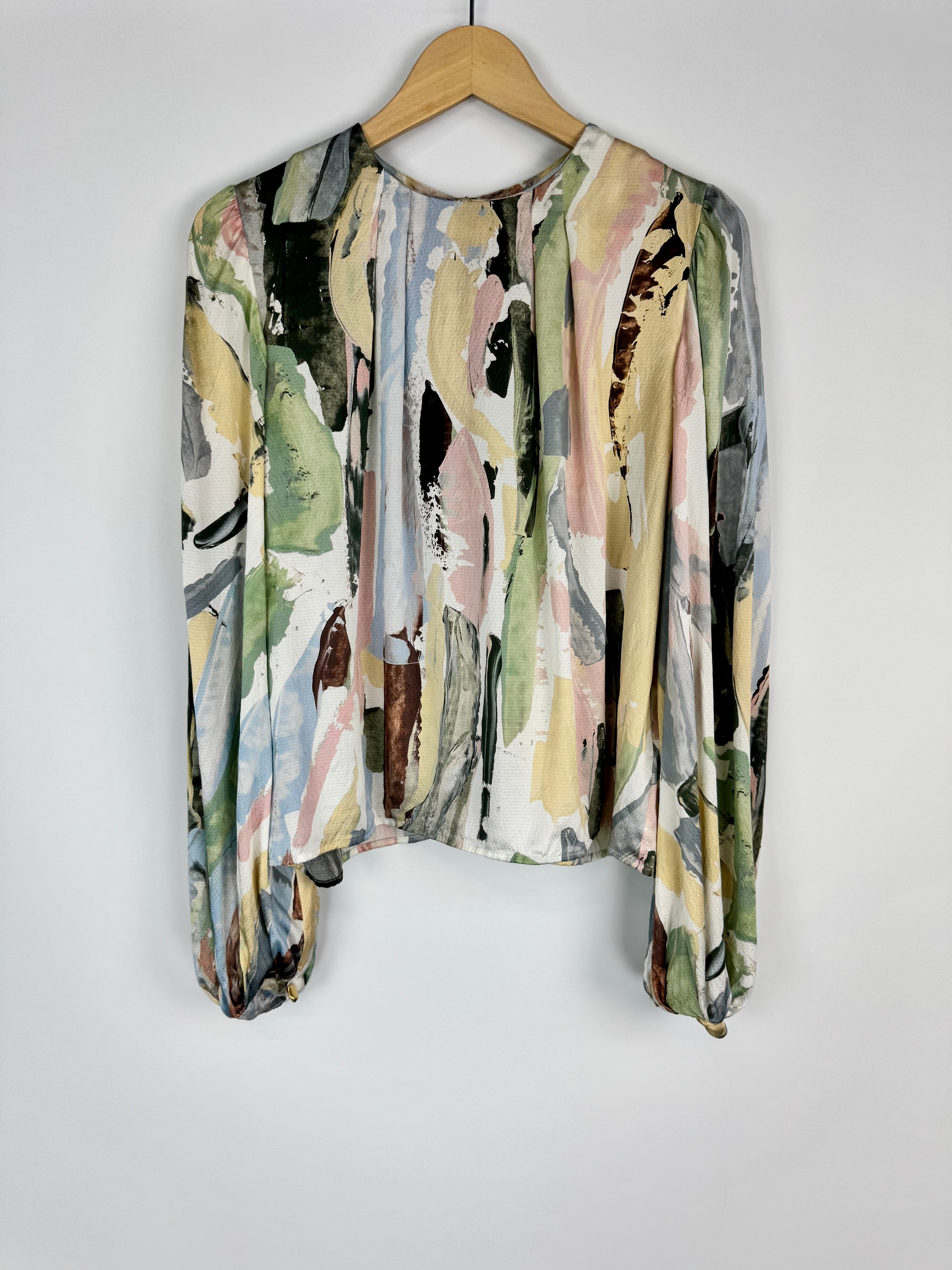 Multicolored patterned blouse on a wooden hanger against a white background