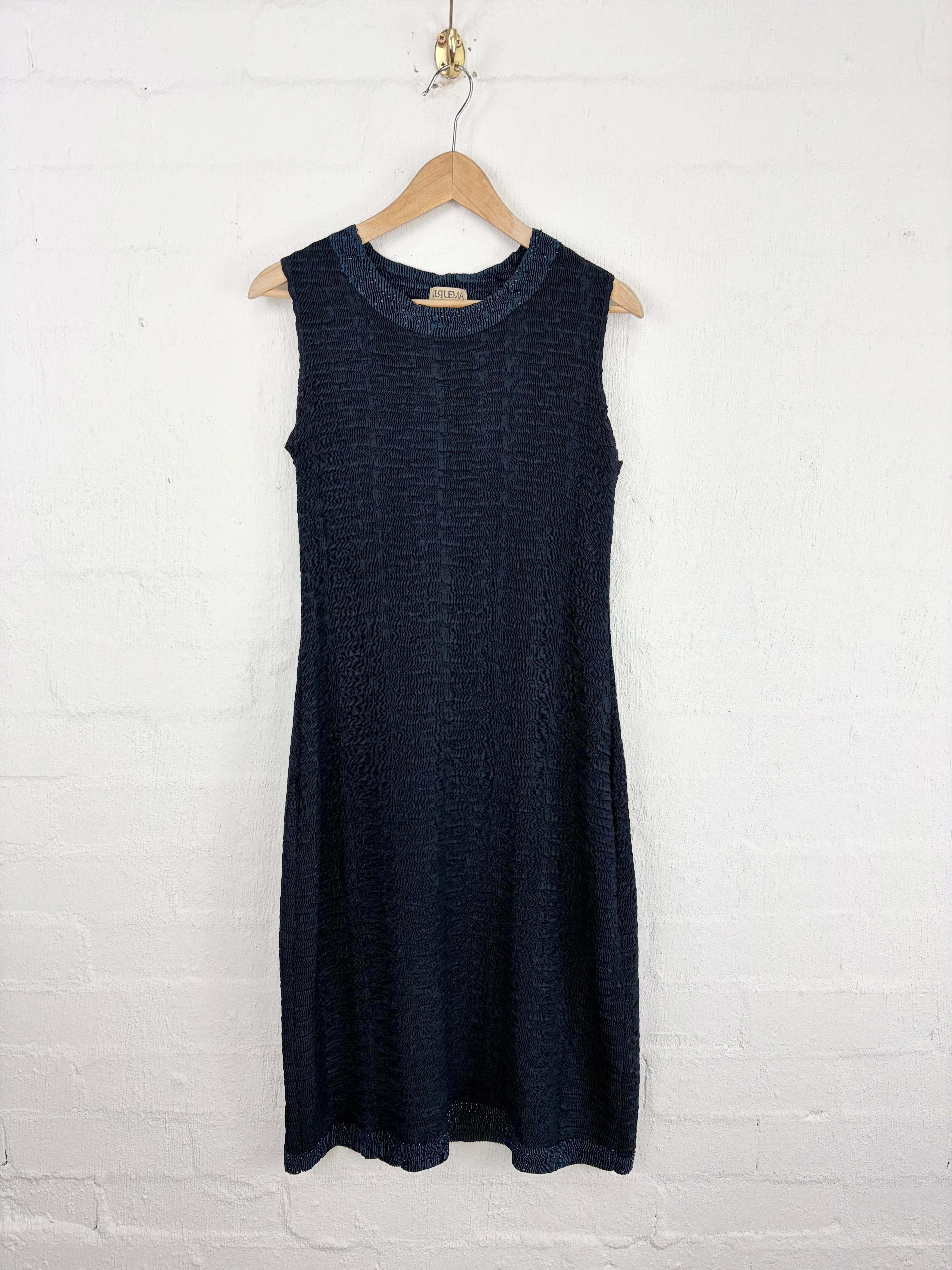 A sleeveless dark navy blue knit dress hanging on a wooden hanger against a white painted brick wall.