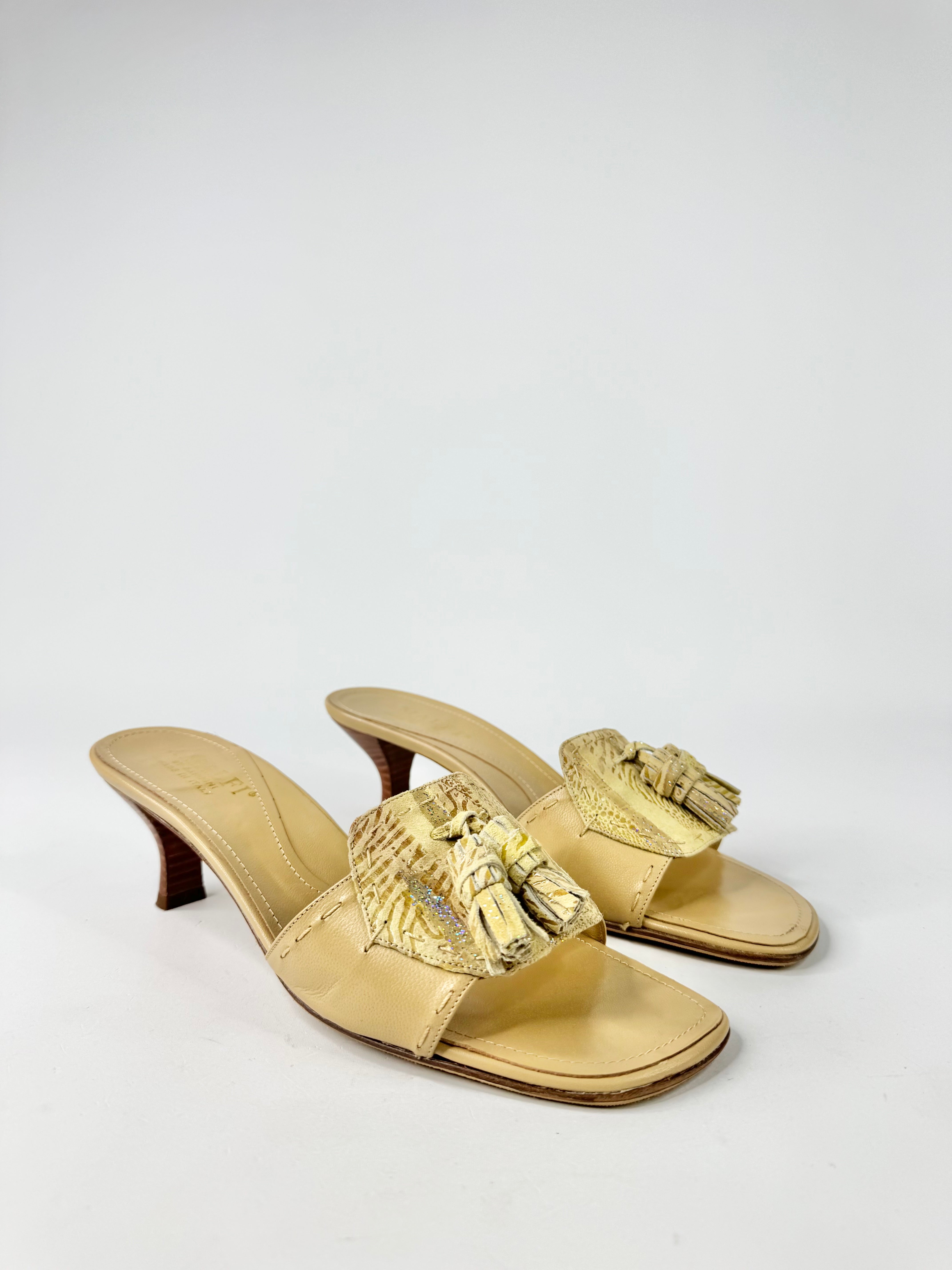 Gold high-heeled sandals with tassel details on a white background