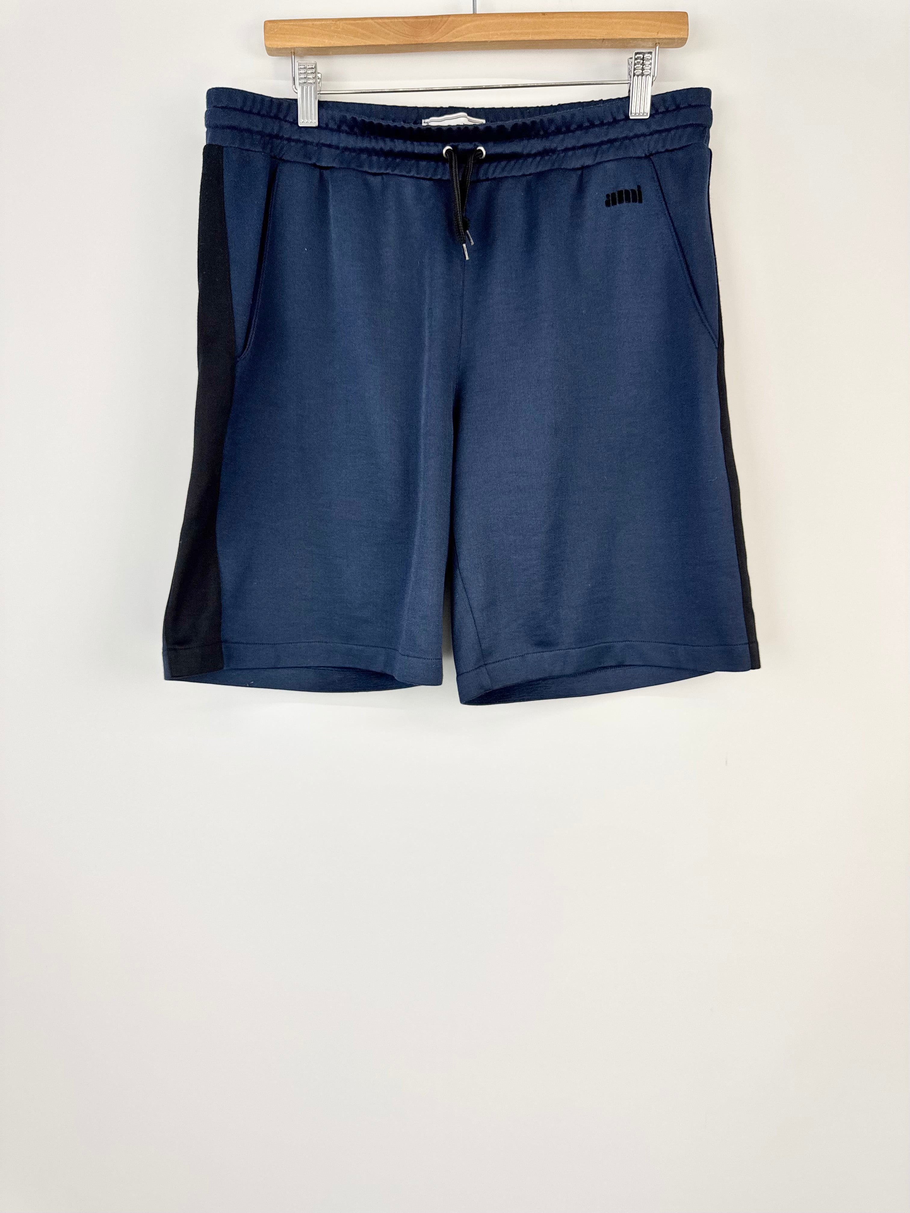 Navy blue shorts hanging on a wooden hanger against a white wall.