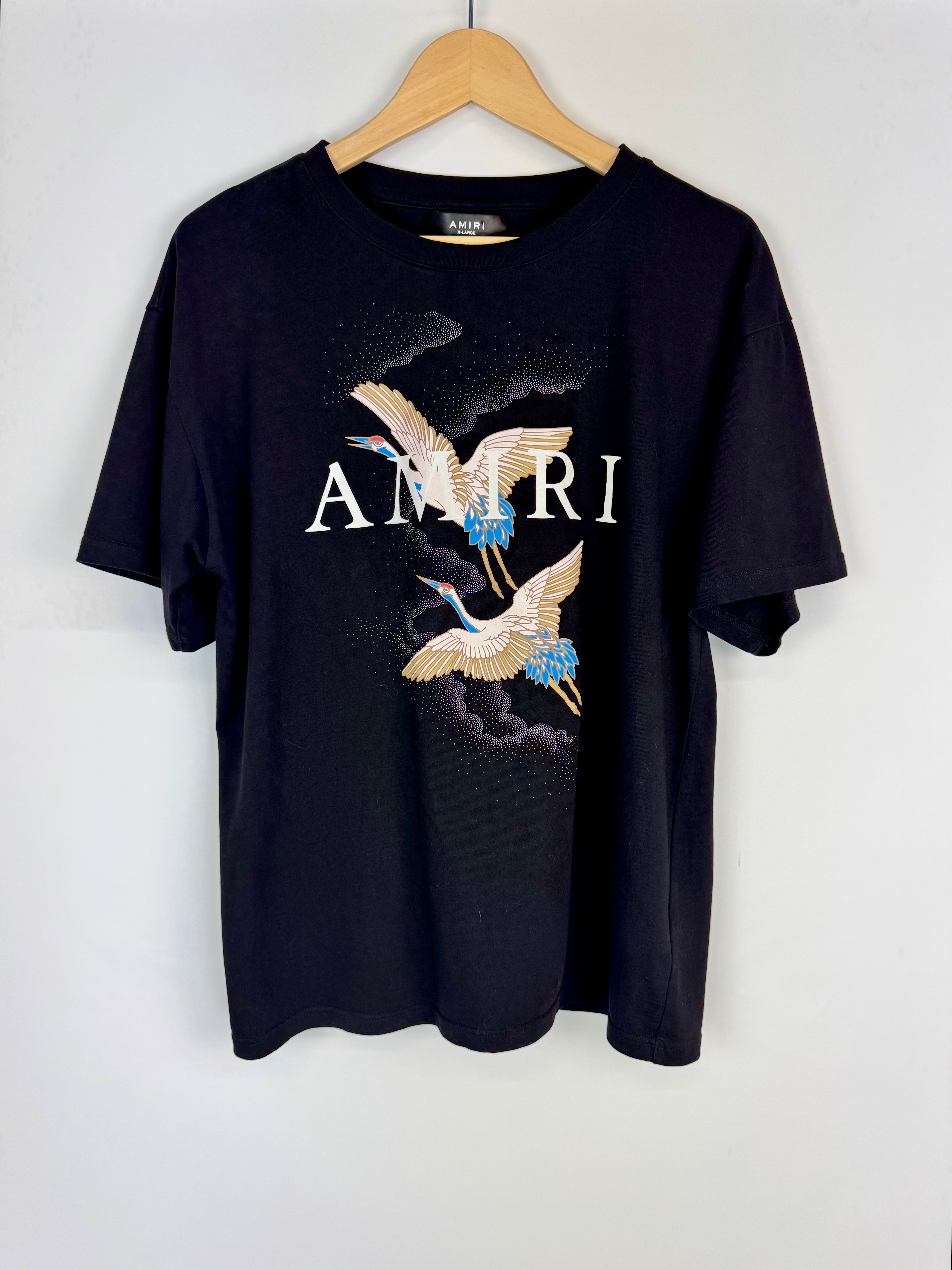 Black t-shirt with 'Amiri' logo and bird design on a hanger against a white background