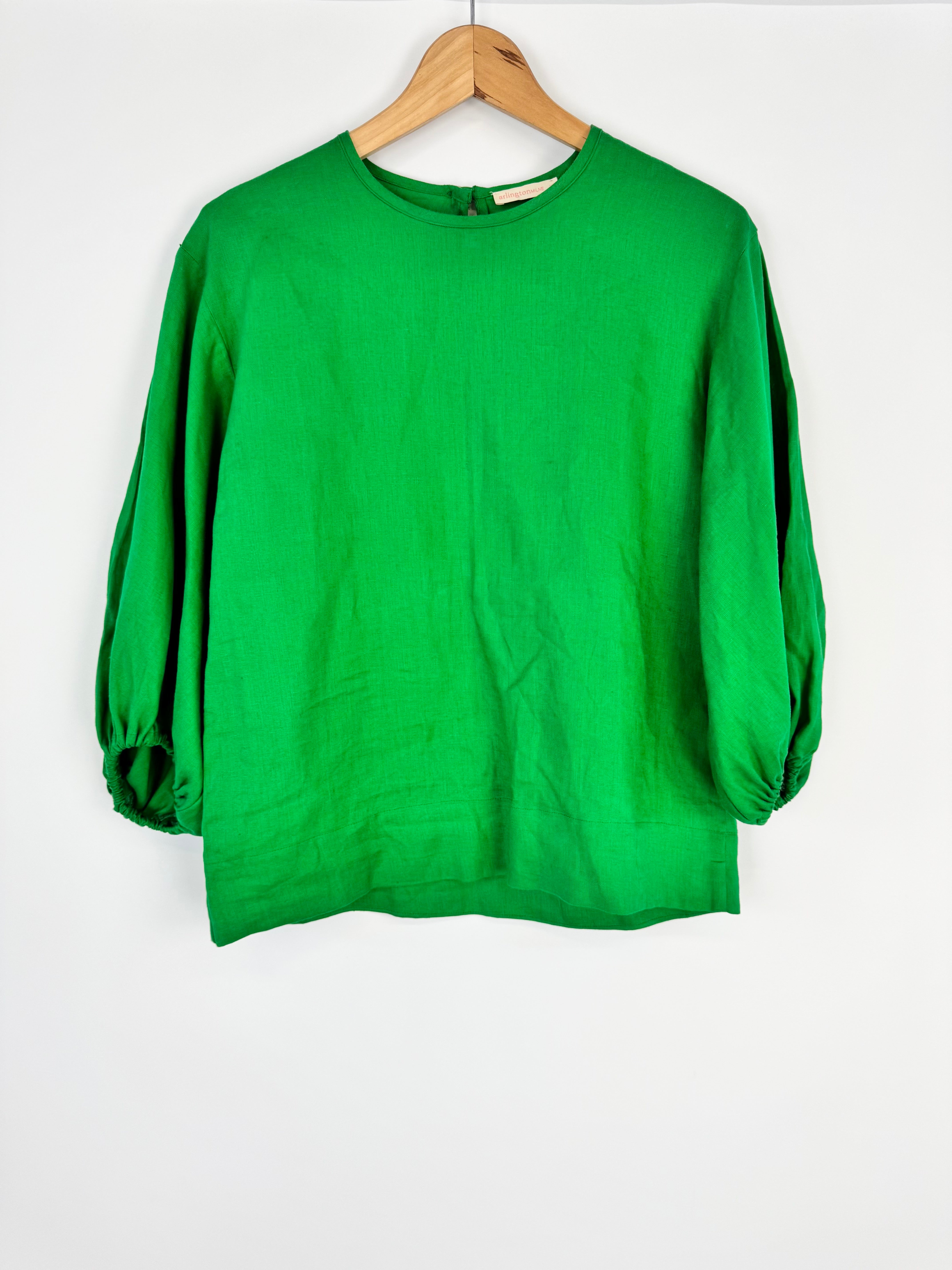 Green blouse on a wooden hanger against a white background