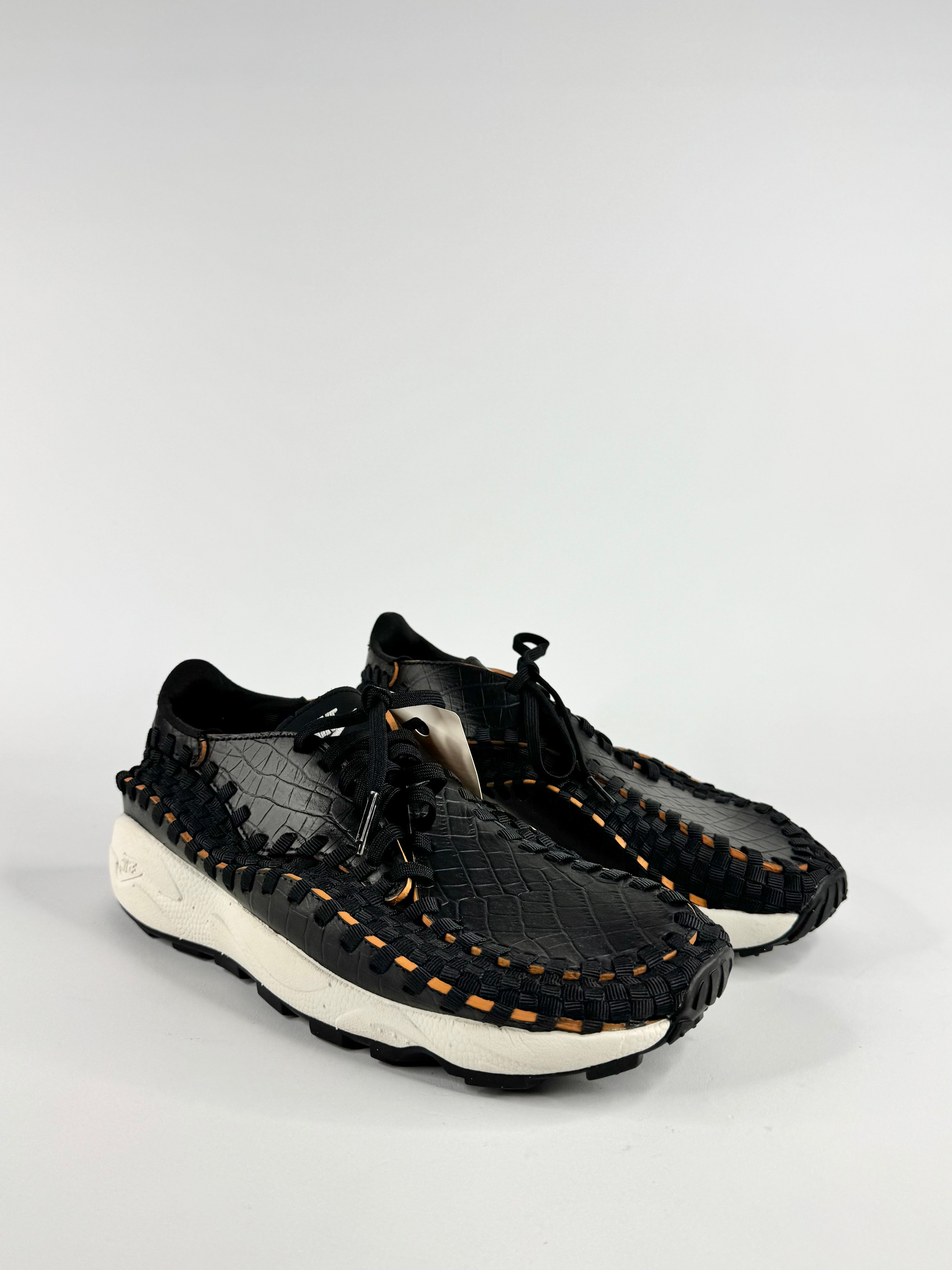 Black woven sneakers with white soles on a light gray background