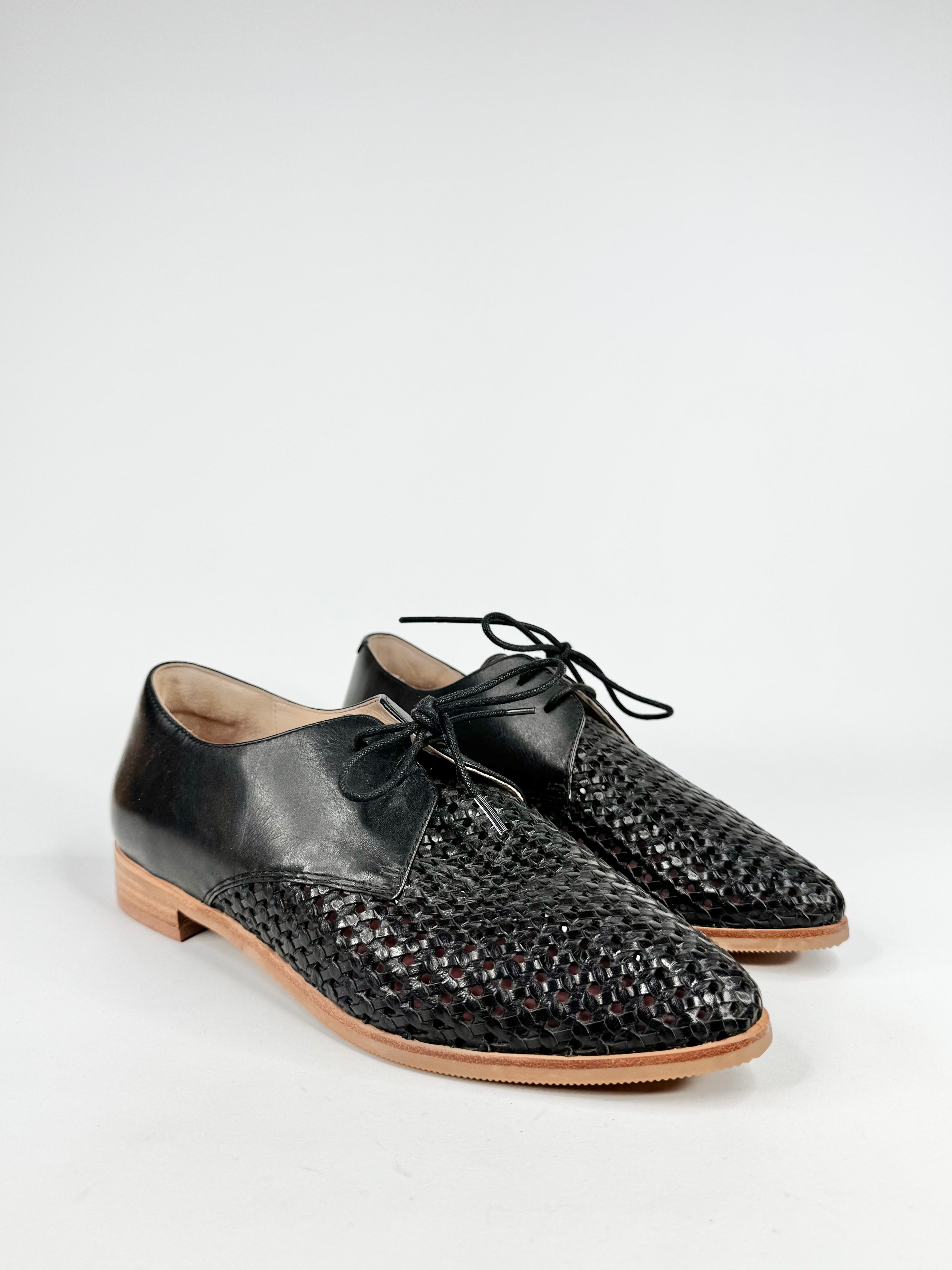 Pair of black leather shoes with woven pattern on a white background