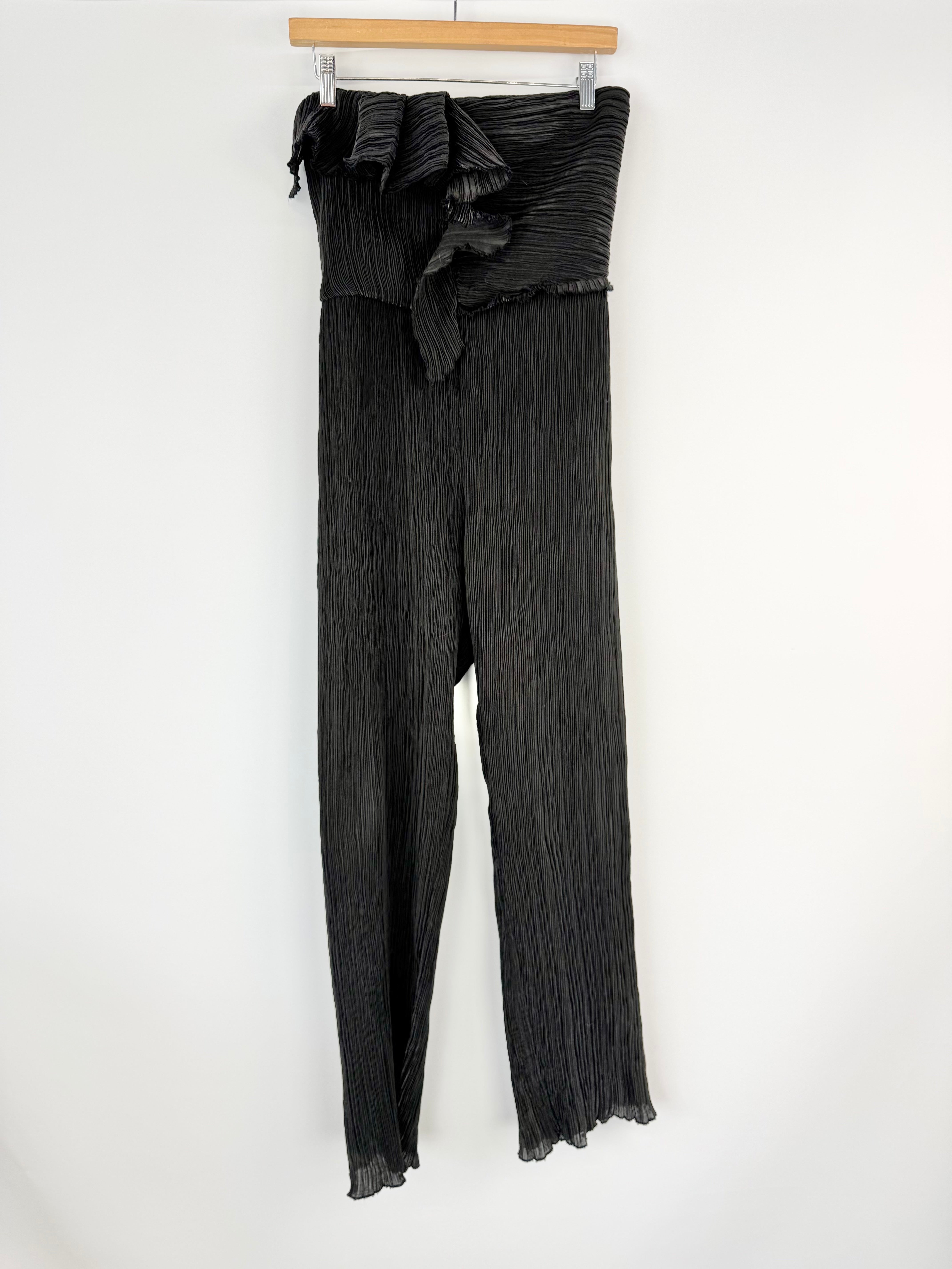 Black pleated sleeveless jumpsuit with ruffled waistband on a hanger against a white background