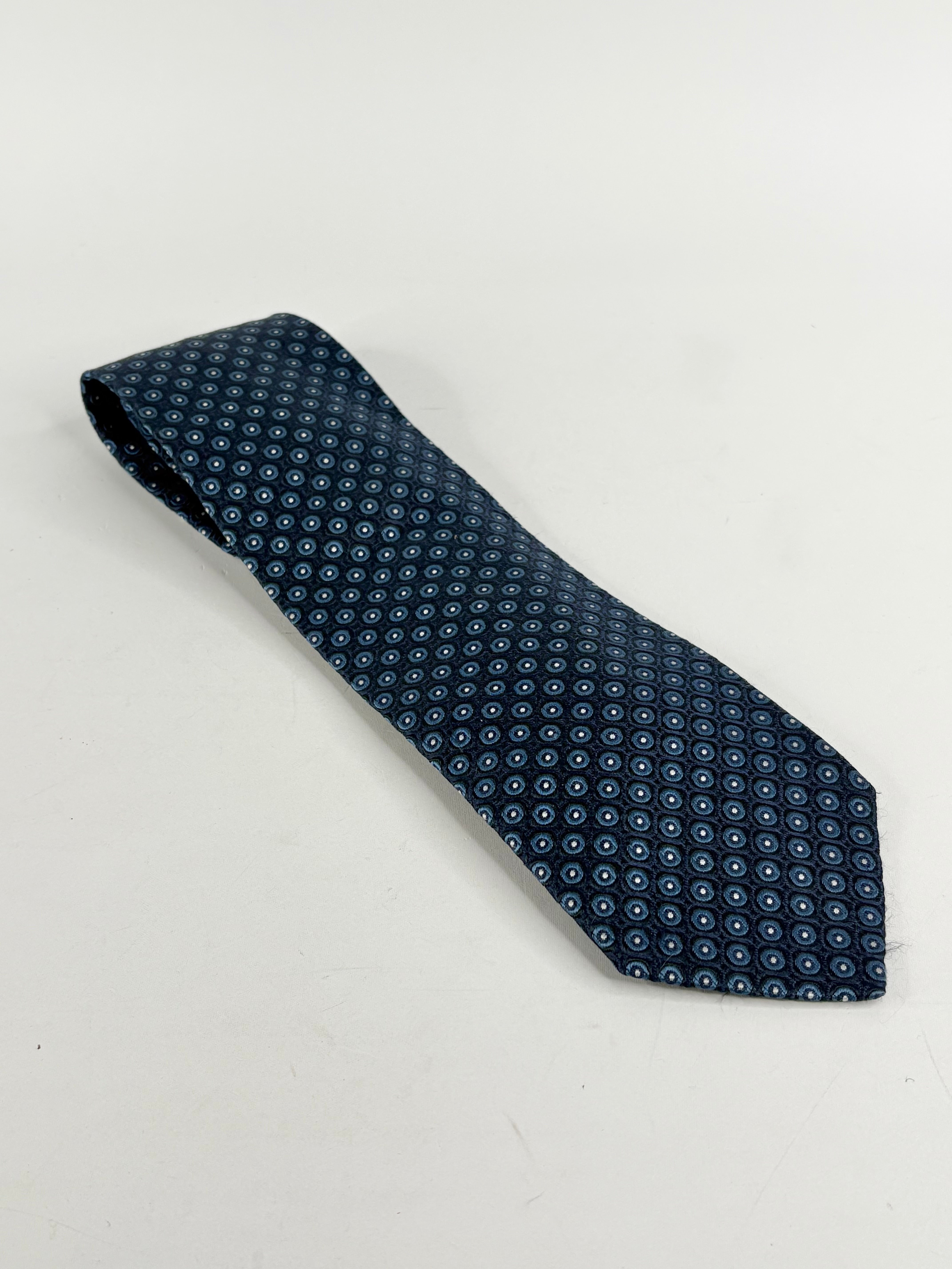 Navy blue silk necktie with a target pattern, laid out on a white background.