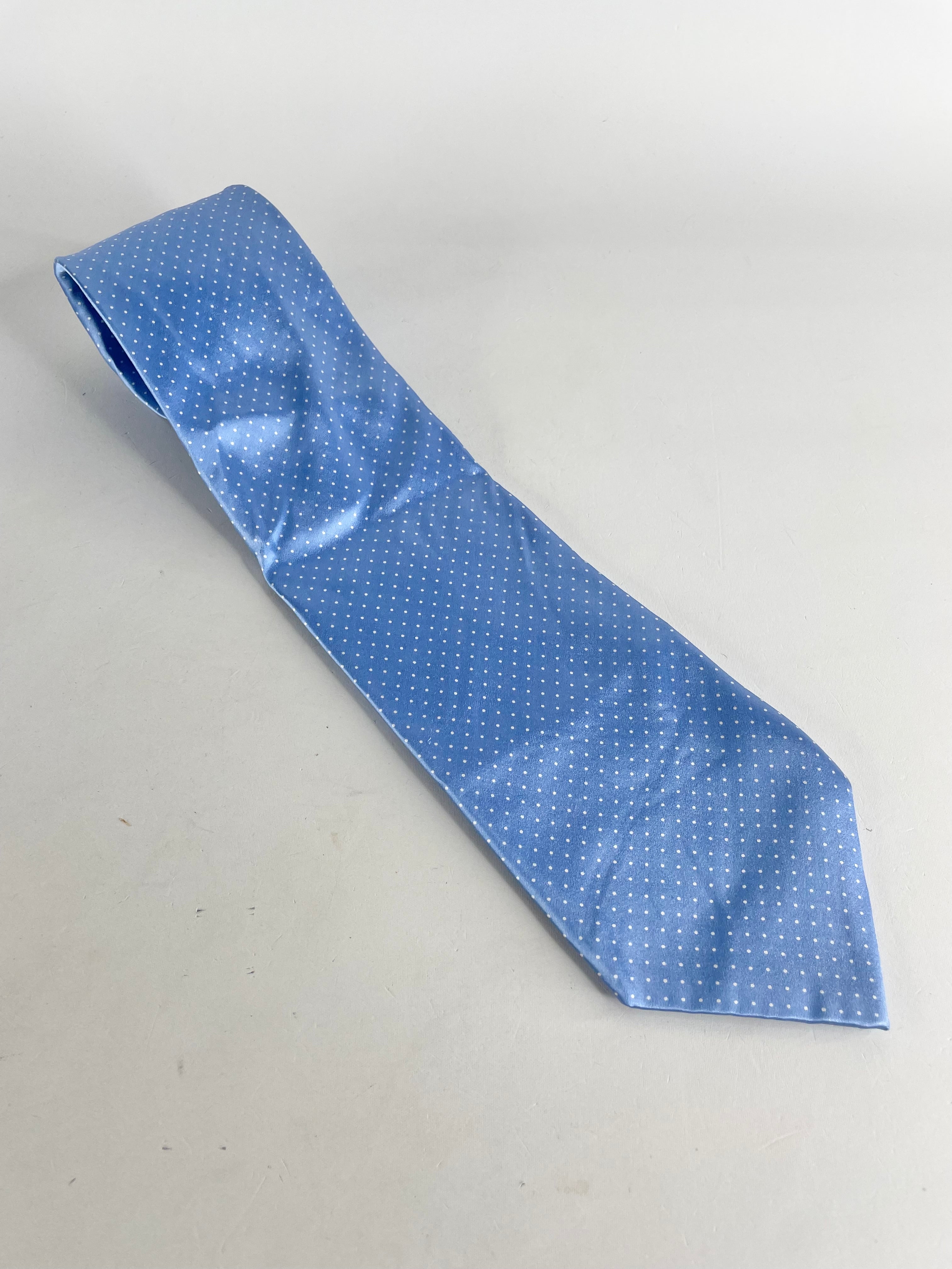 A blue dotted satin silk tie laid out on a plain surface.