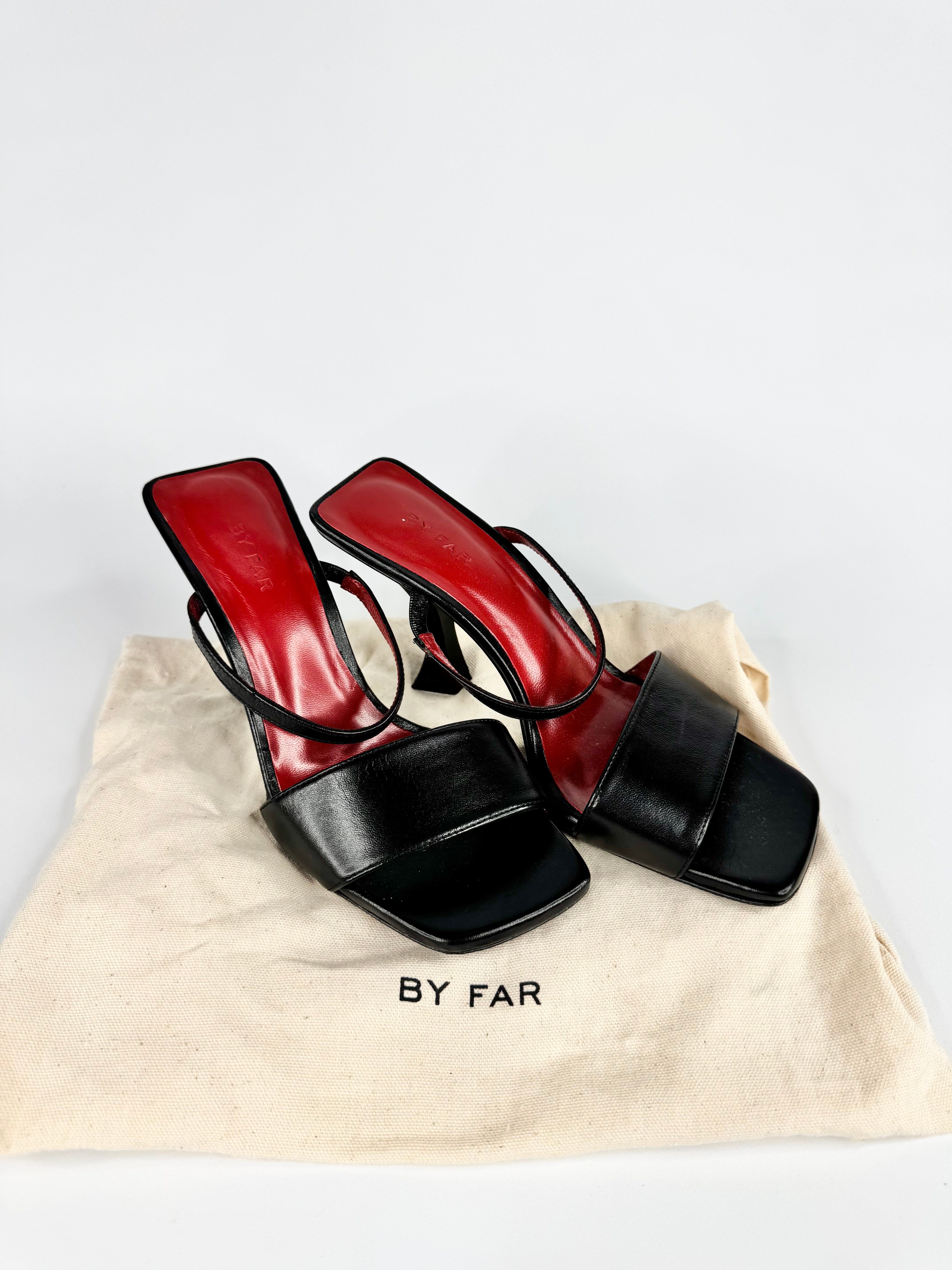 Red and black high-heeled shoes on a beige 'By Far' dust bag against a white background