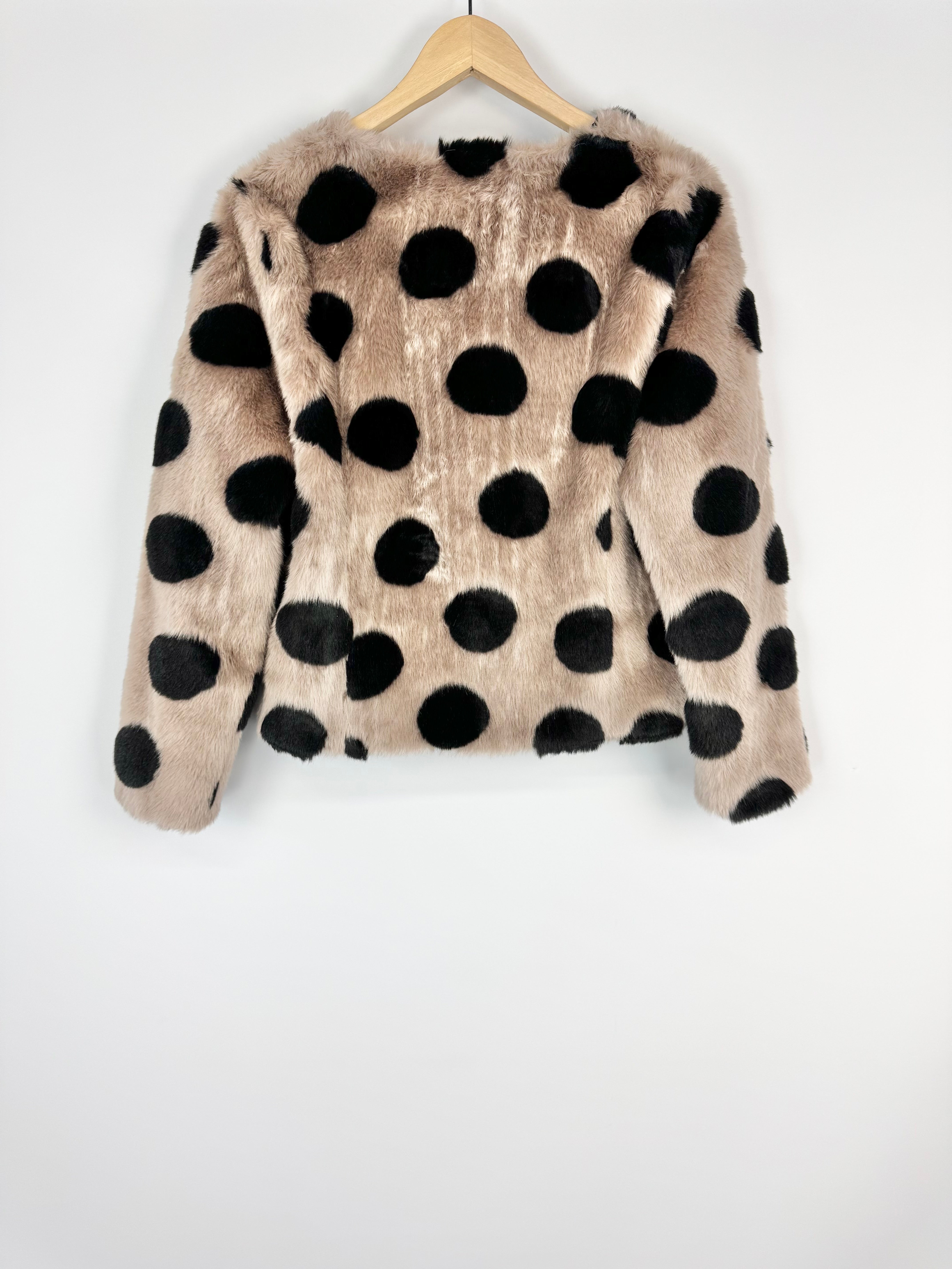 Beige jacket with black polka dots on a wooden hanger against a white background