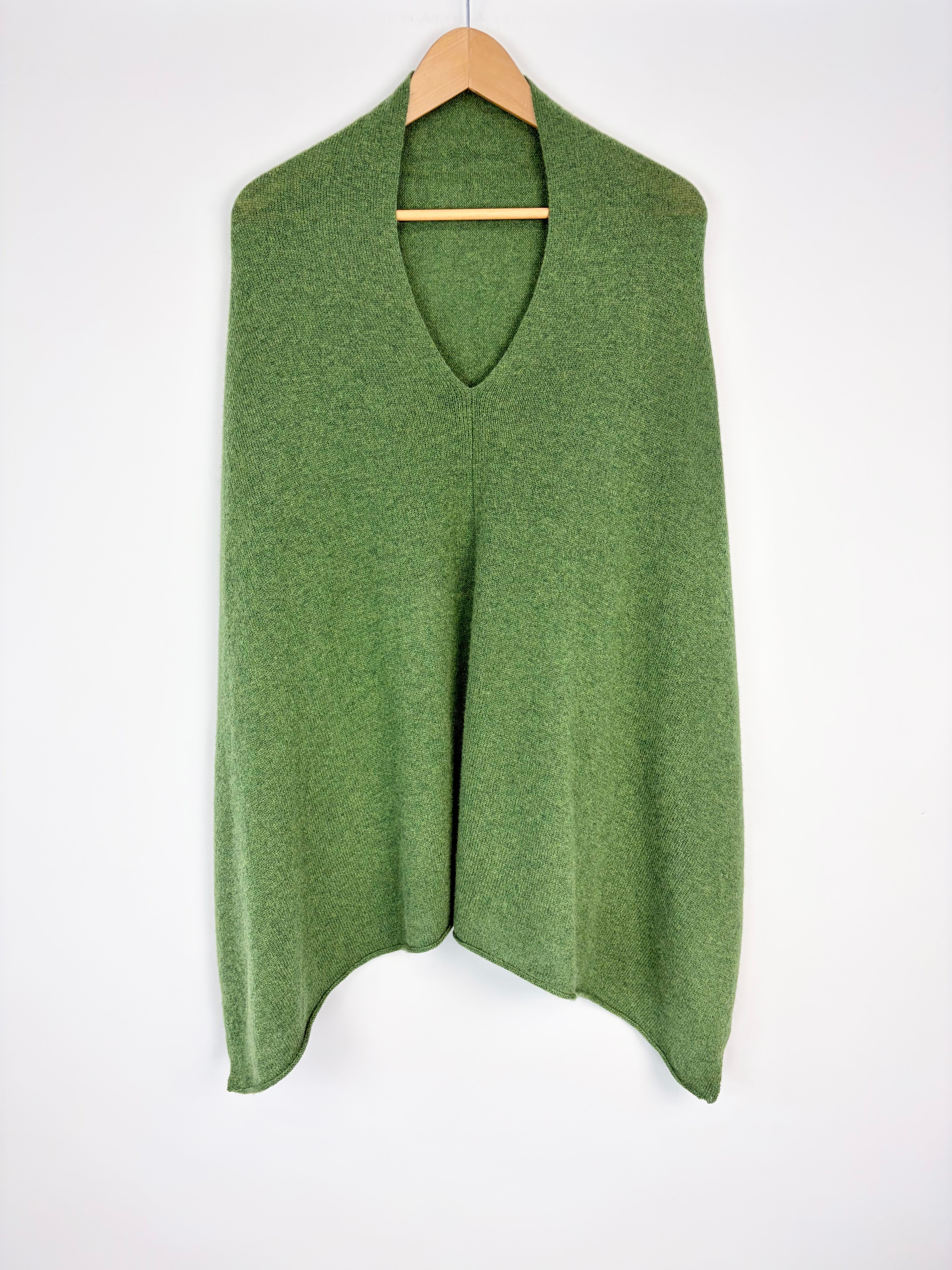 Green sweater vest on a wooden hanger against a white background