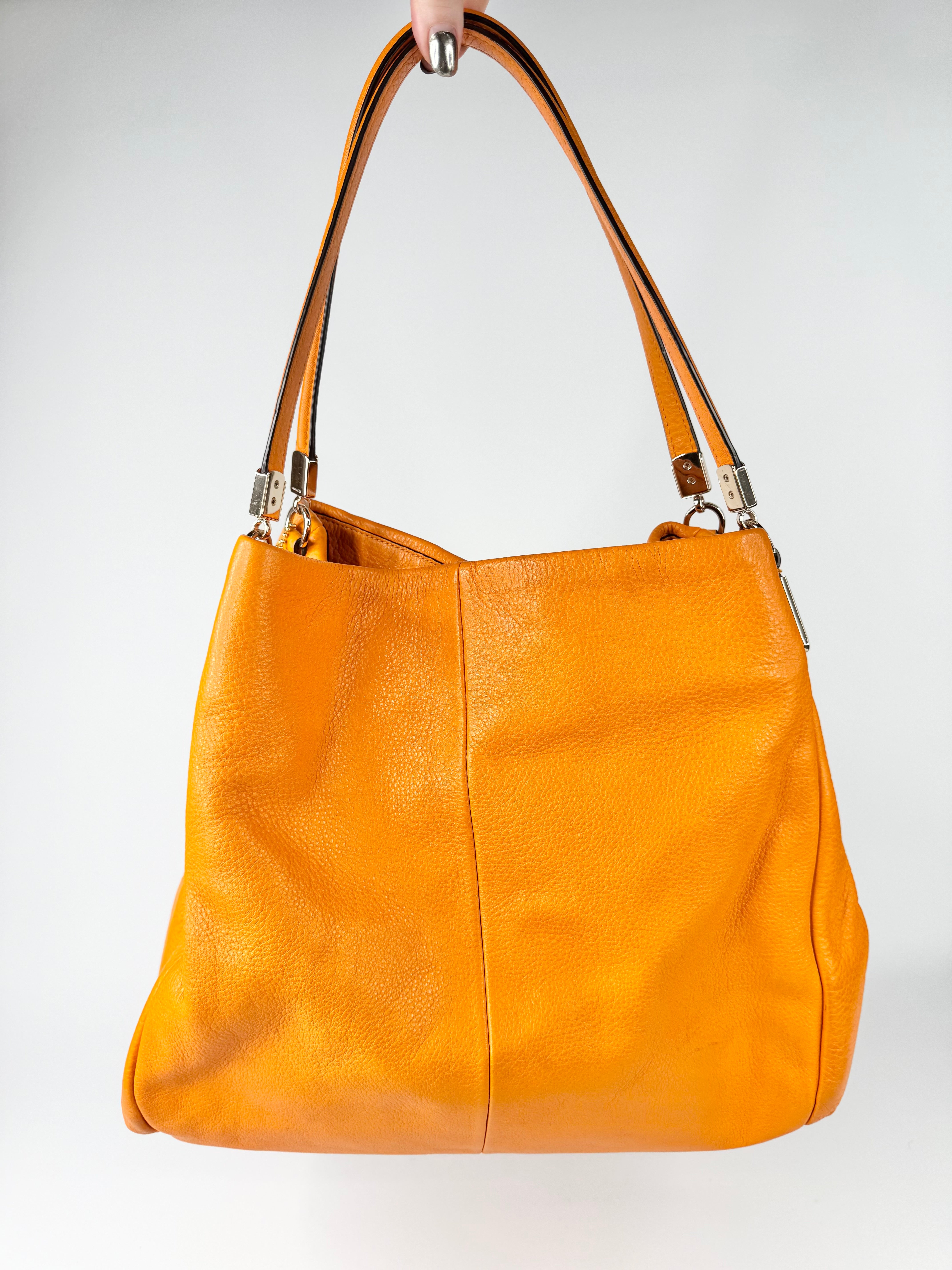 orange handbag held by a hand against a white background