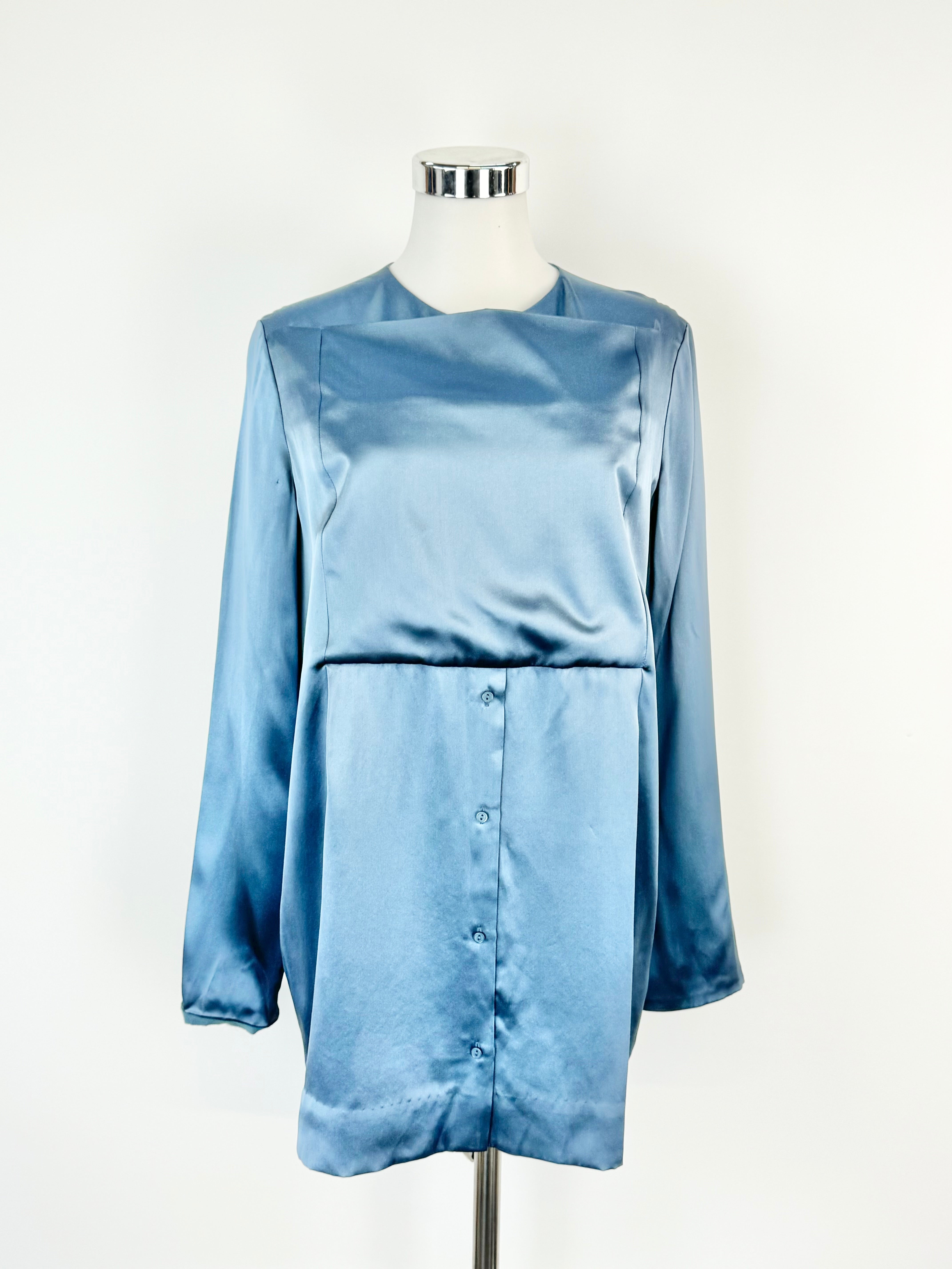 A blue silk blouse with a high rounded neckline and front panel featuring buttons, displayed on a mannequin.