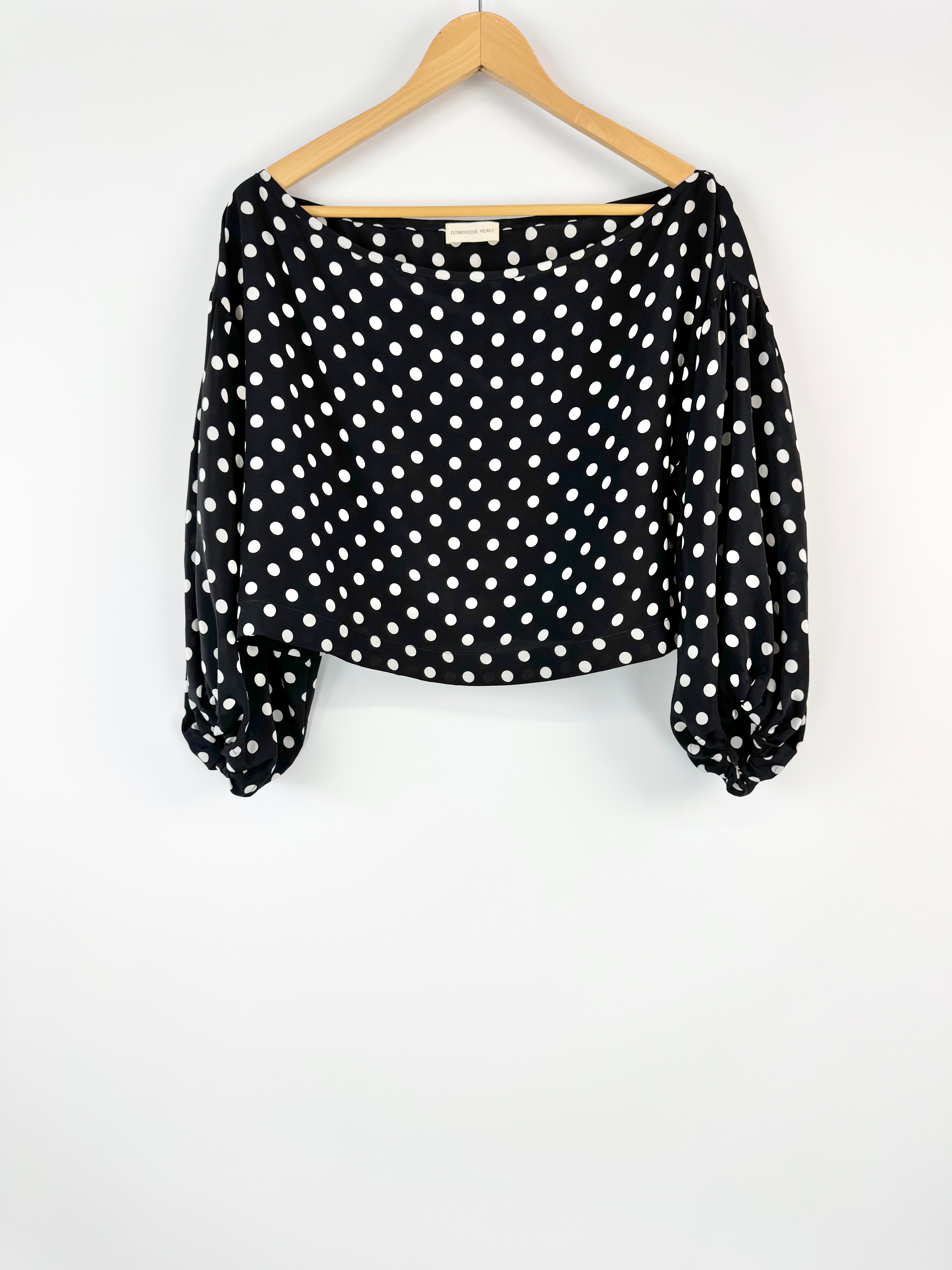 Black blouse with white polka dots on a hanger against a white background