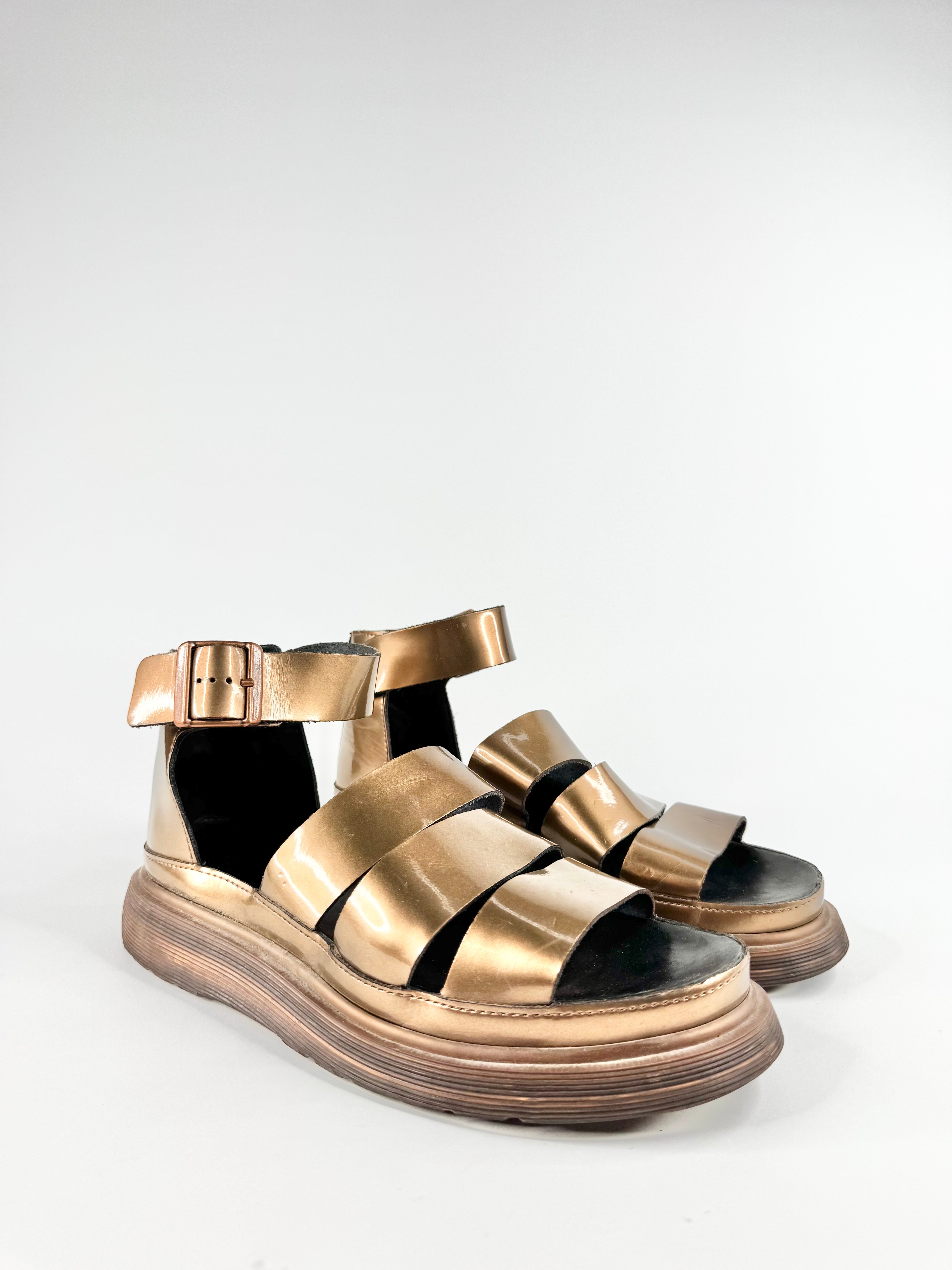 Gold sandals with black soles on a white background