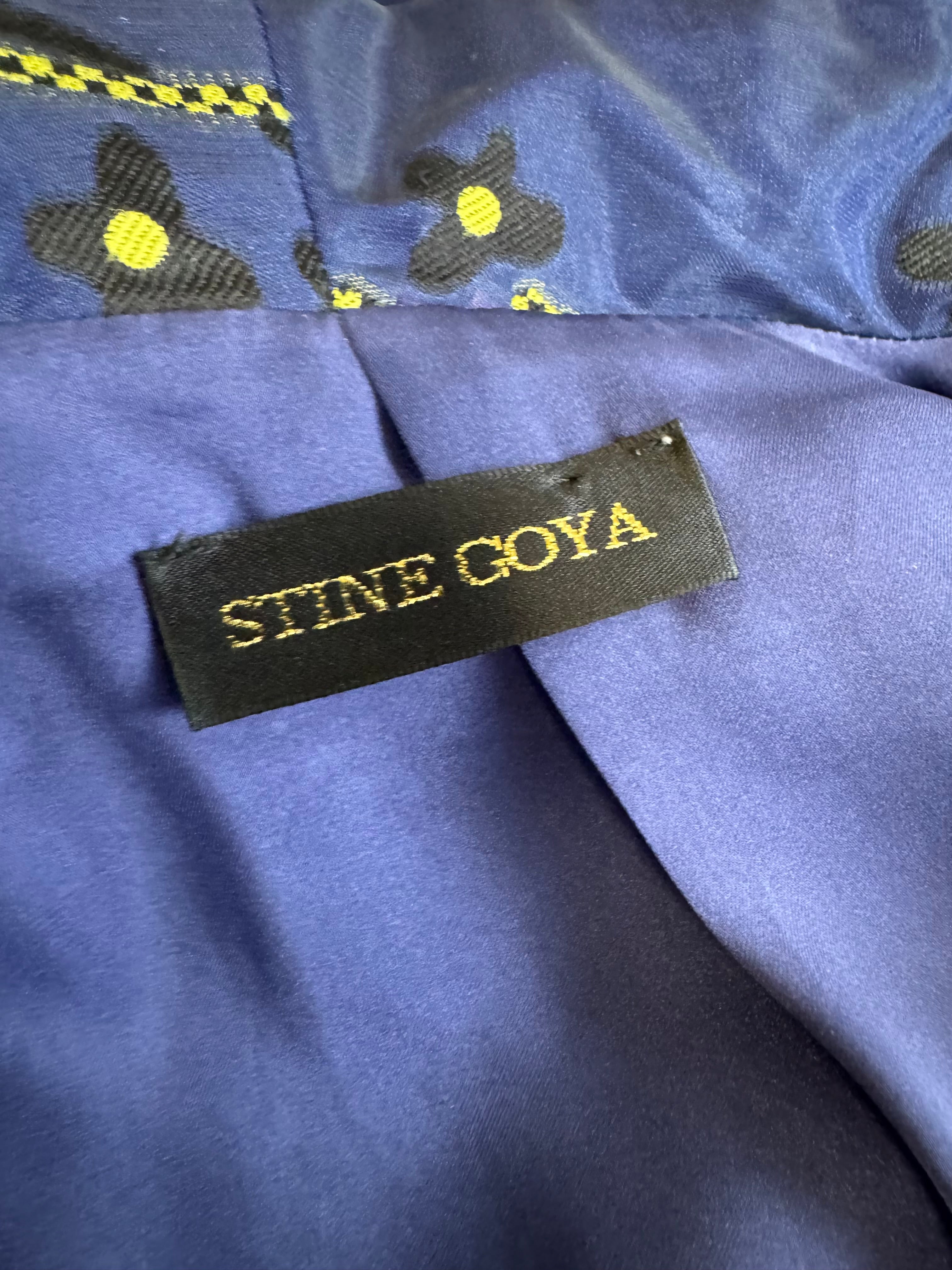 Close-up of a blue fabric with embroidered flowers and a 'Stine Goya' label.