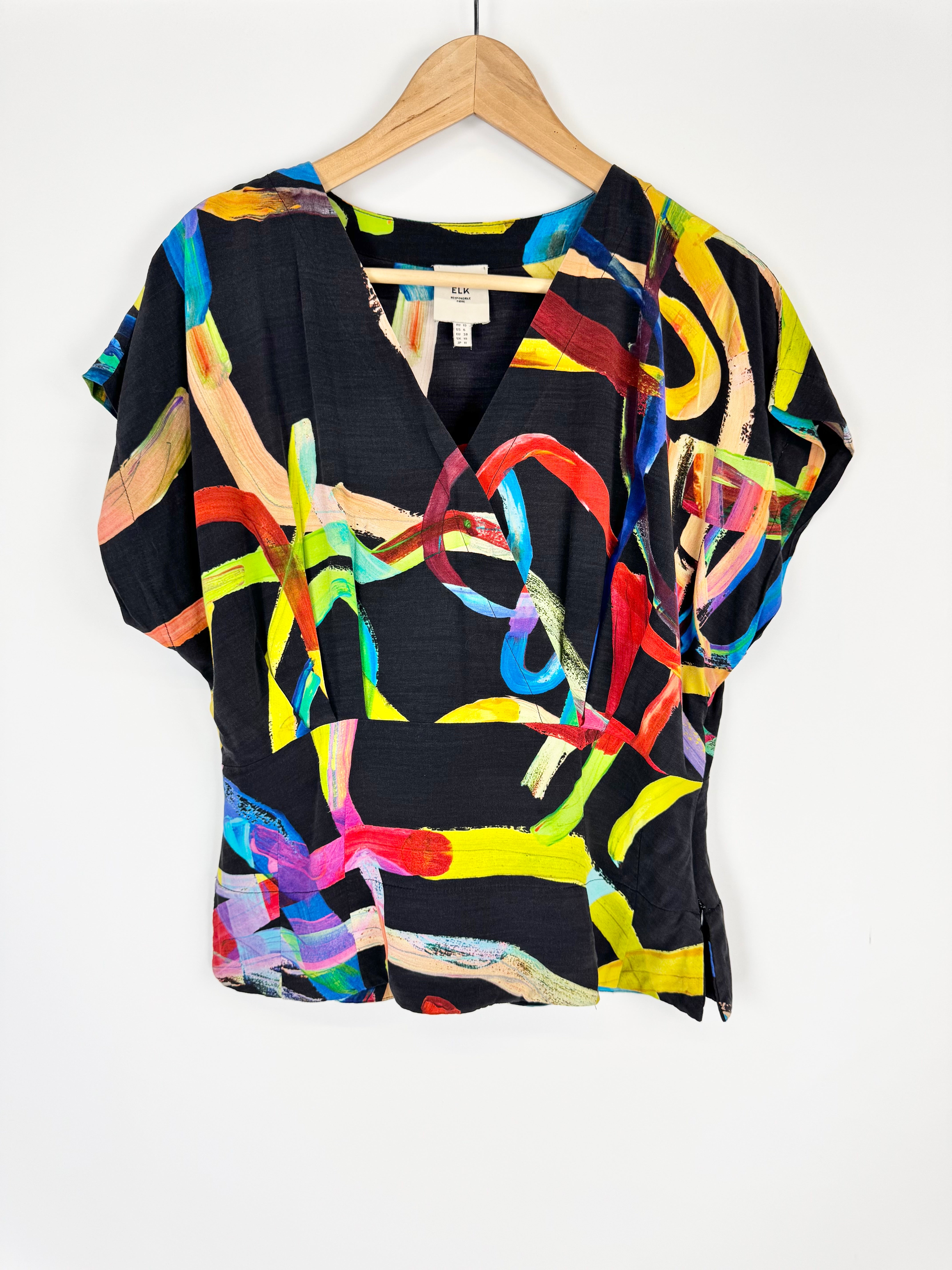 Colorful abstract-patterned top on a hanger against a white background