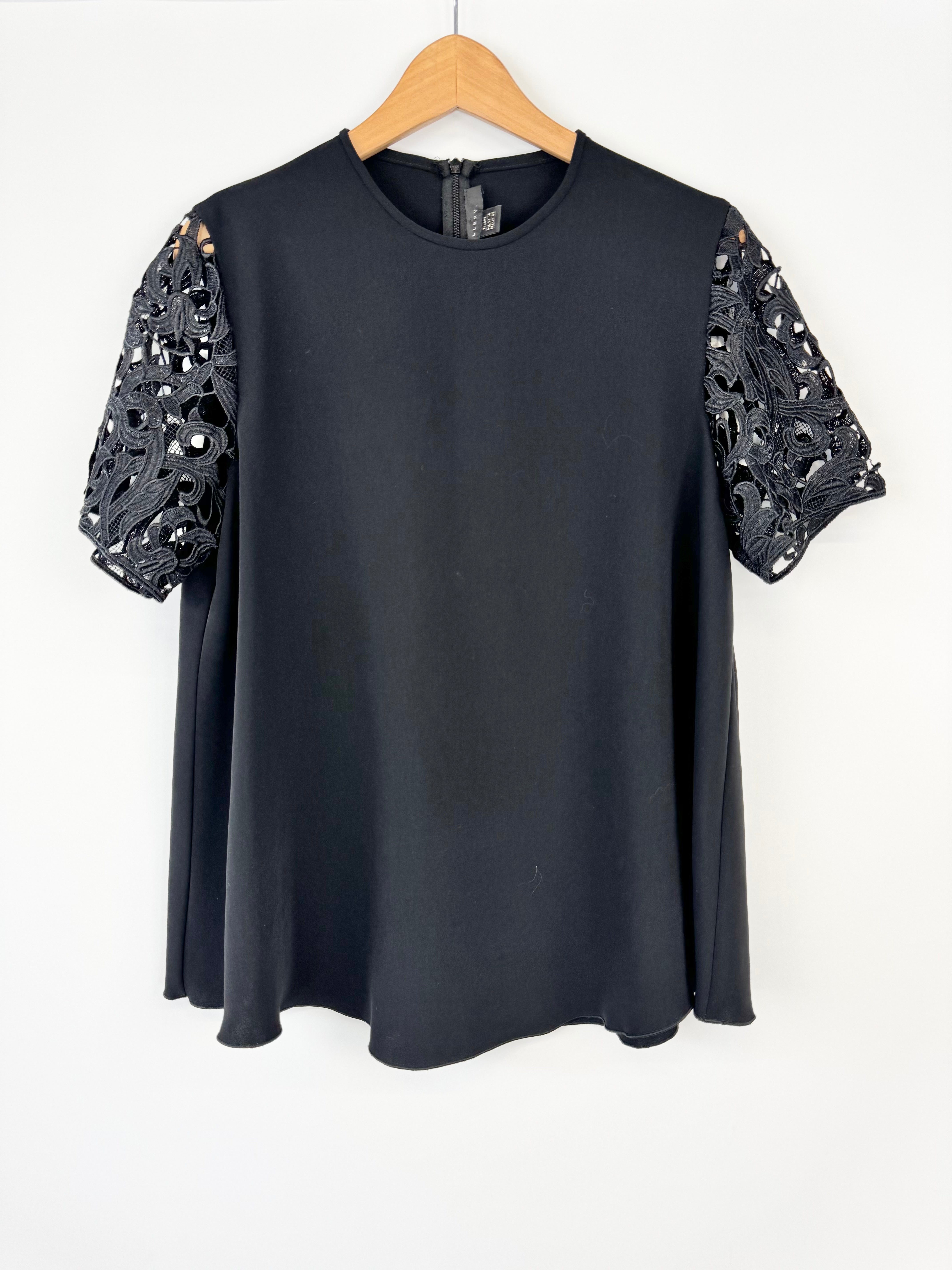 Black top with lace sleeves on a wooden hanger against a white background