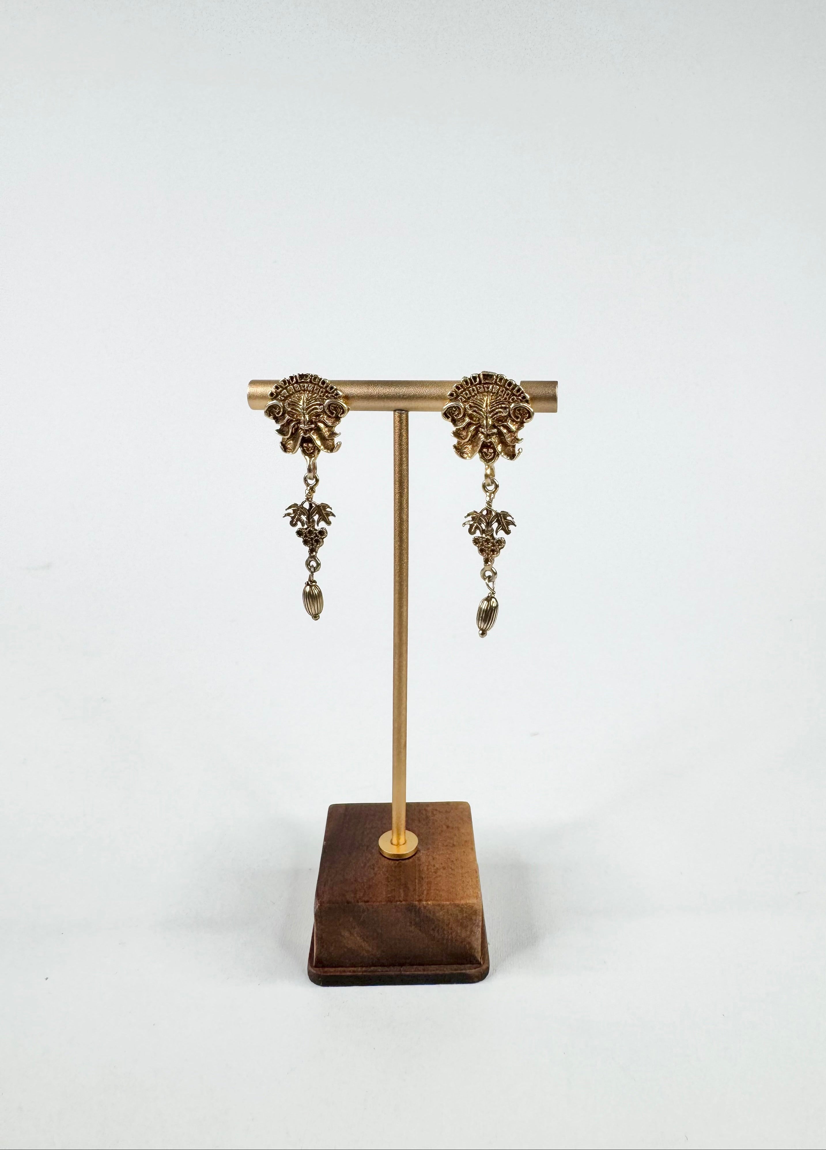 Pair of gold earrings on a wooden stand against a white background