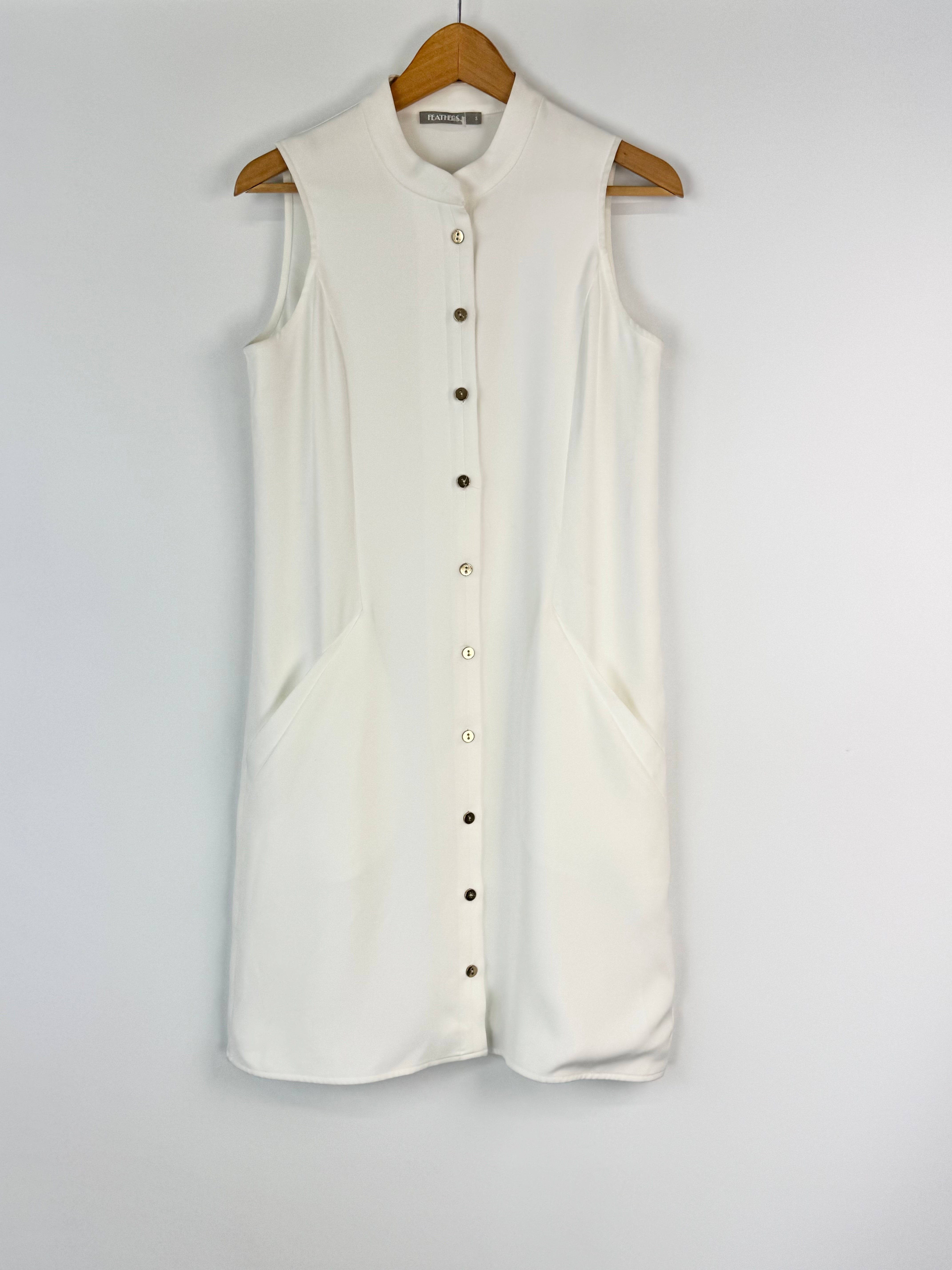White sleeveless button-up shirt on a wooden hanger against a white background