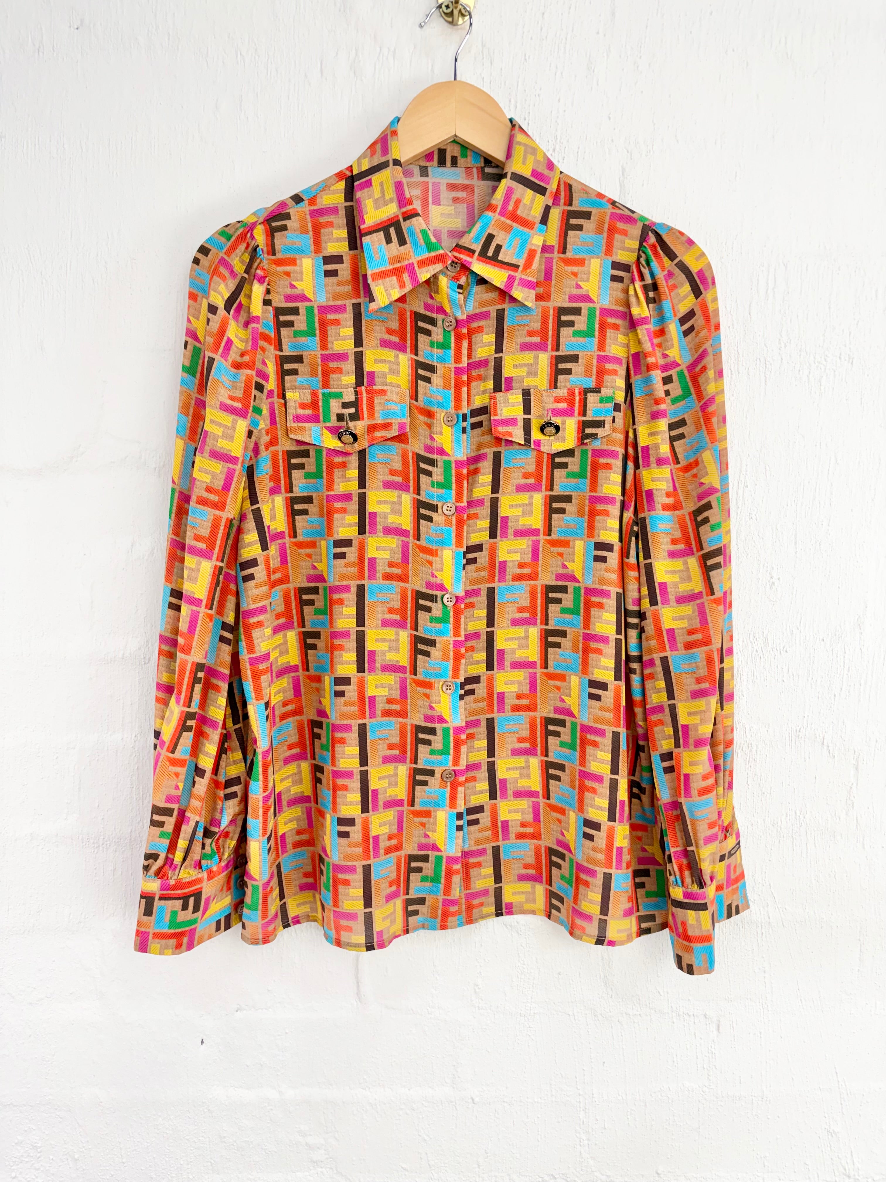 A long-sleeve button-up shirt with a colorful geometric Fendi Zucca monogram pattern, hanging on a wooden hanger against a white painted brick wall.