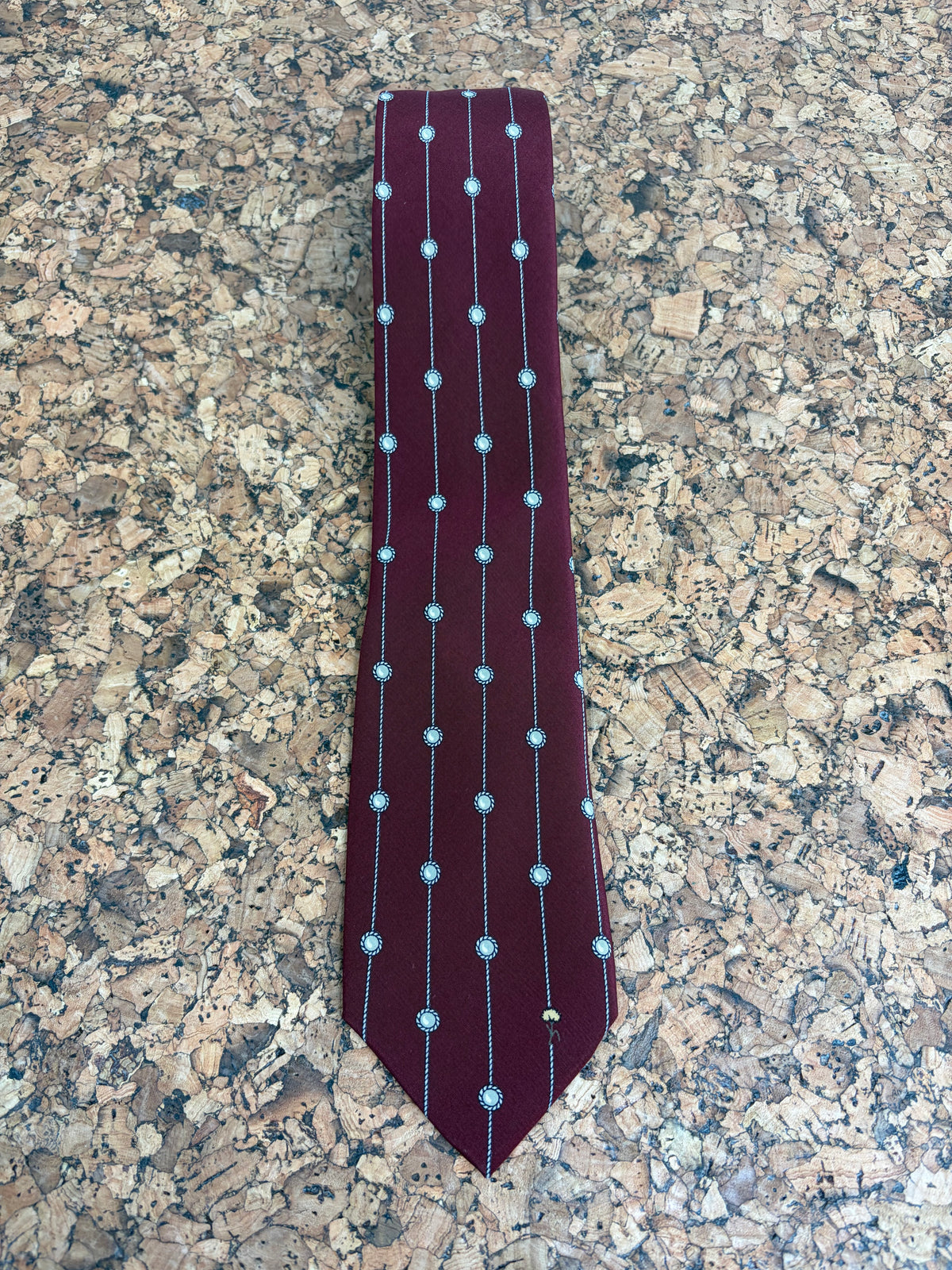 A burgundy necktie with vertical silver stripes and circular silver dot patterns, laid flat on a speckled brown and beige granite countertop.