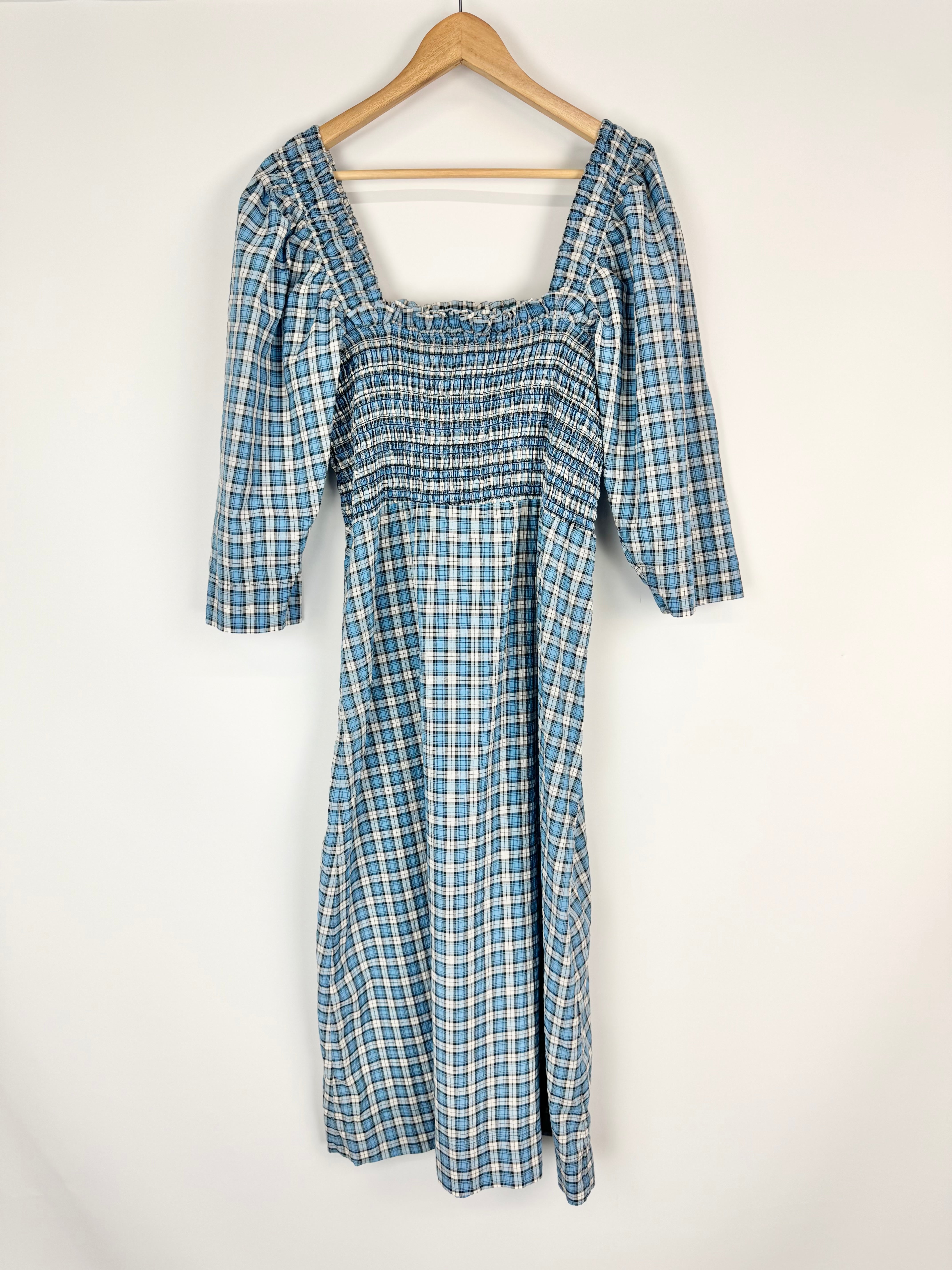 Blue and white checkered dress on a wooden hanger against a white background