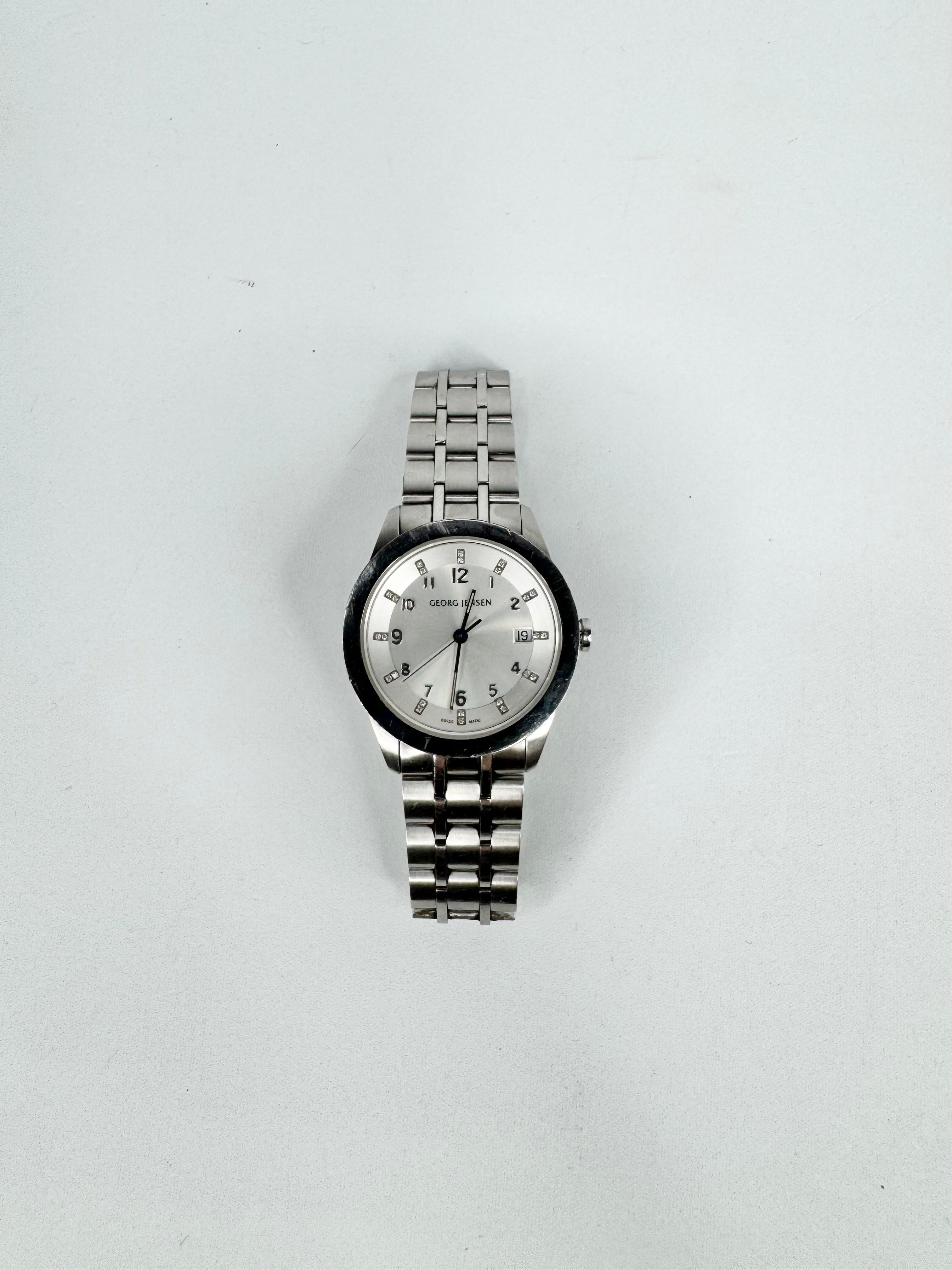 Silver wristwatch with a white face on a light gray background