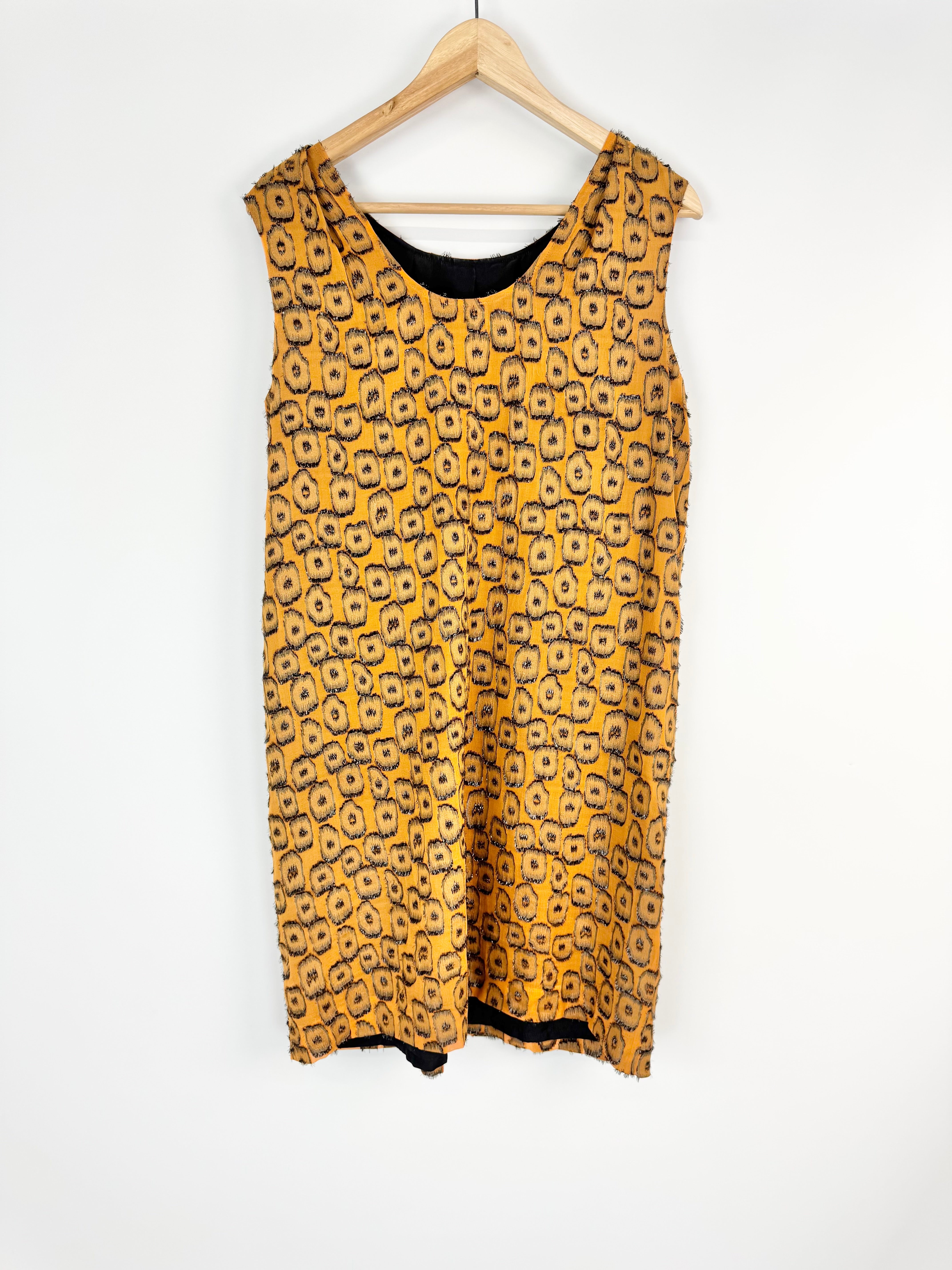 Yellow patterned dress on a hanger against a white background