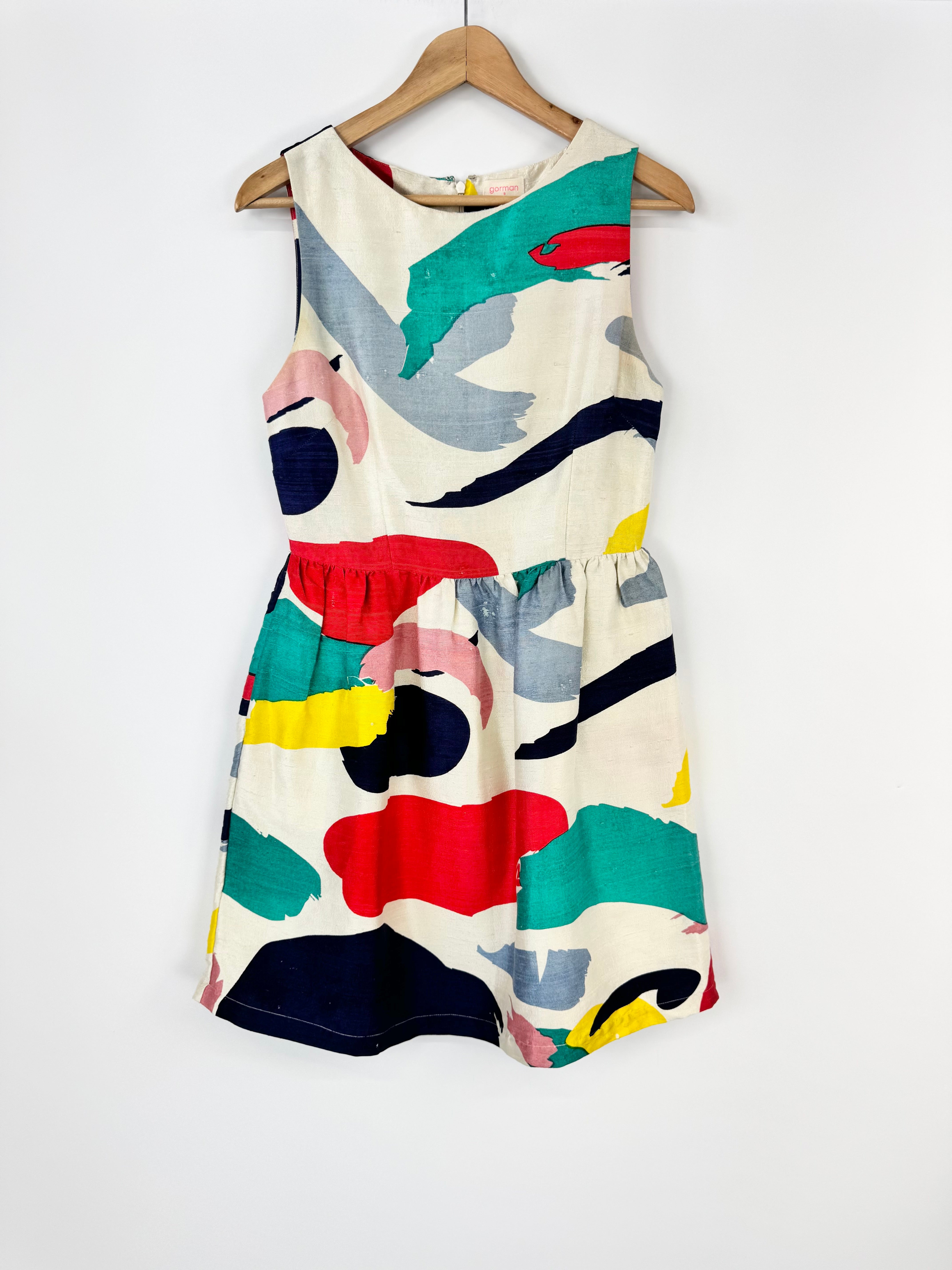 Colorful sleeveless dress with abstract patterns on a hanger against a white background