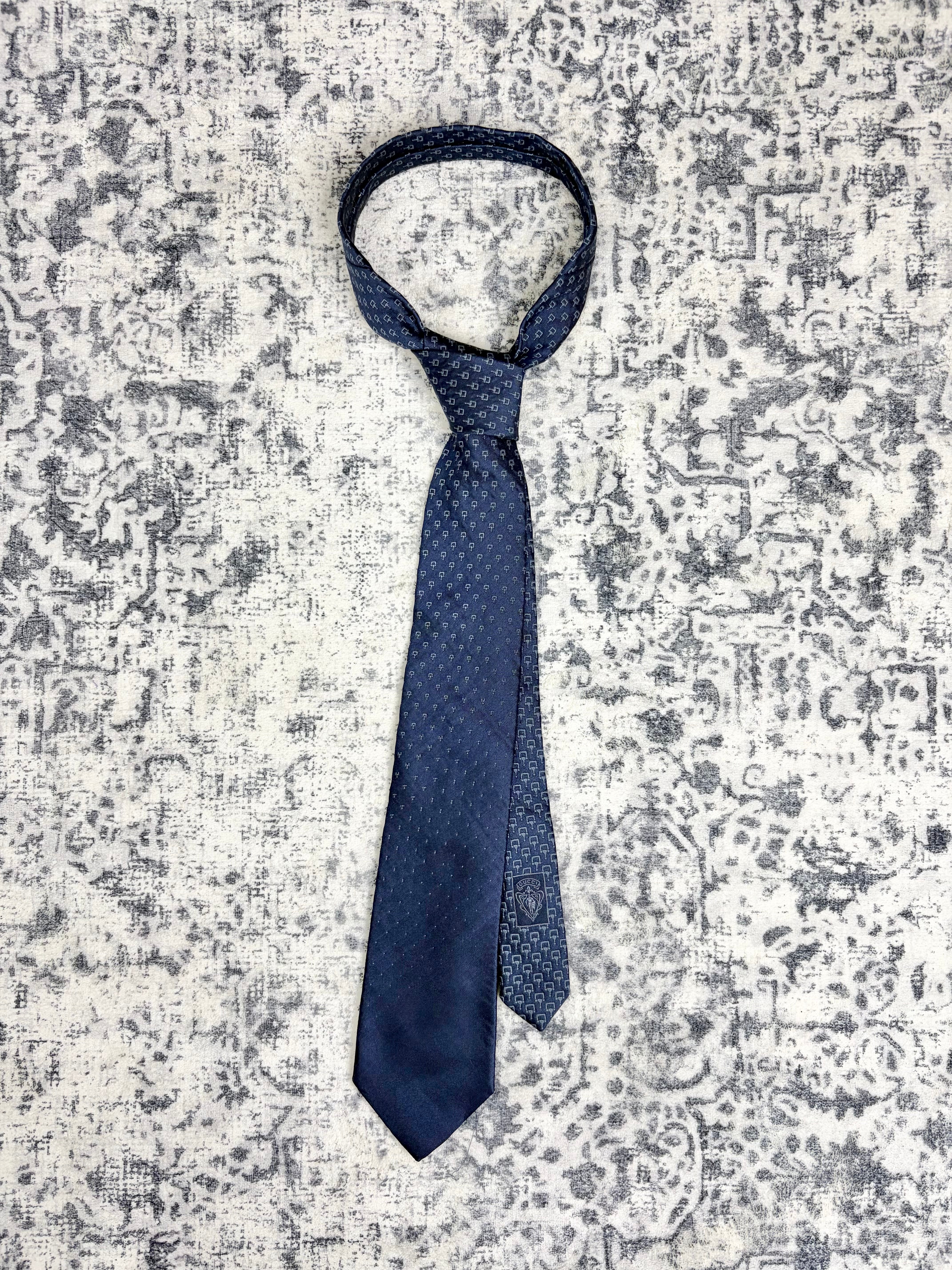 A dark blue necktie with a subtle geometric pattern, laid flat on a distressed gray and white patterned fabric background.