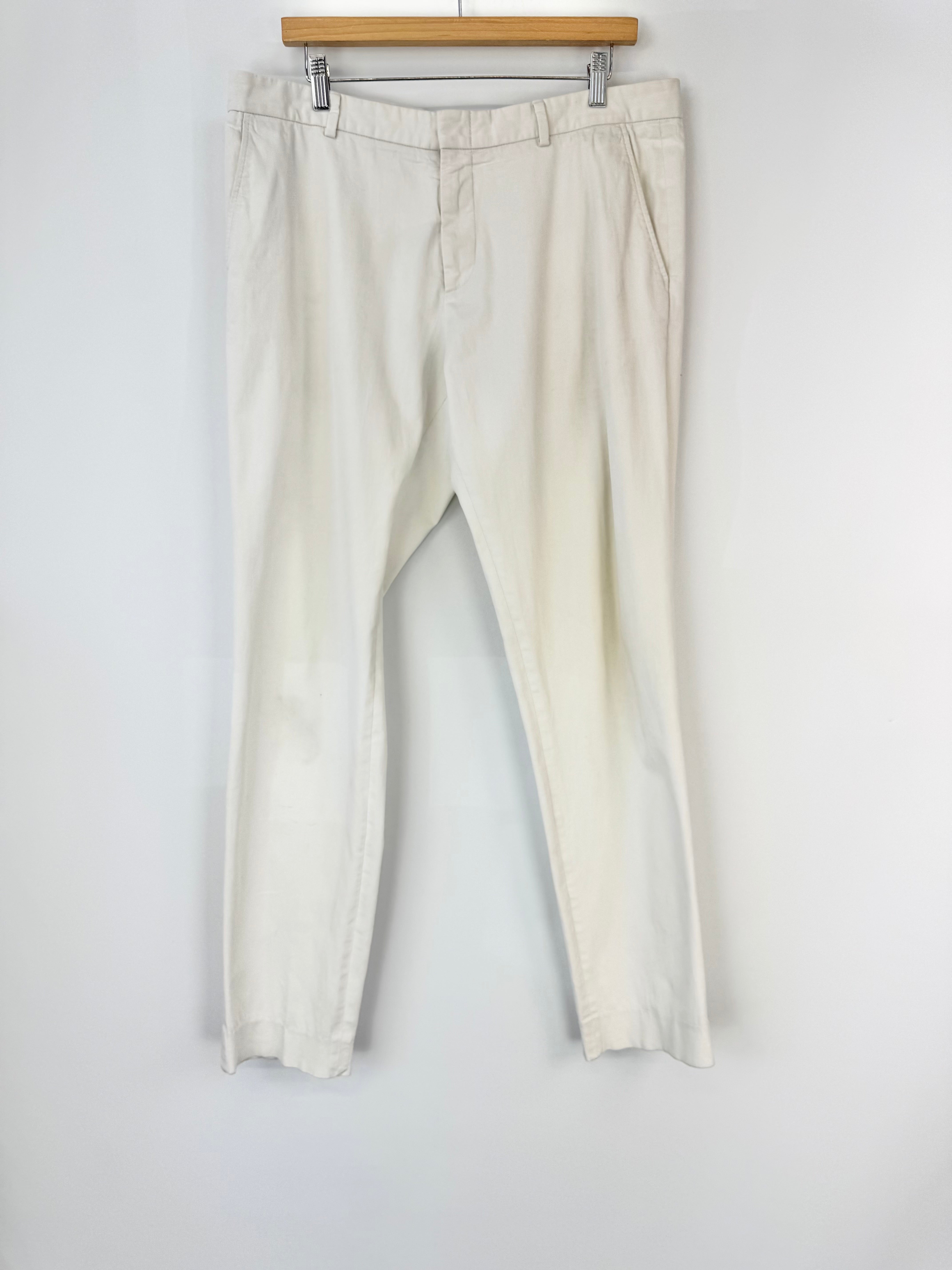 White pants hanging on a wooden hanger against a white wall