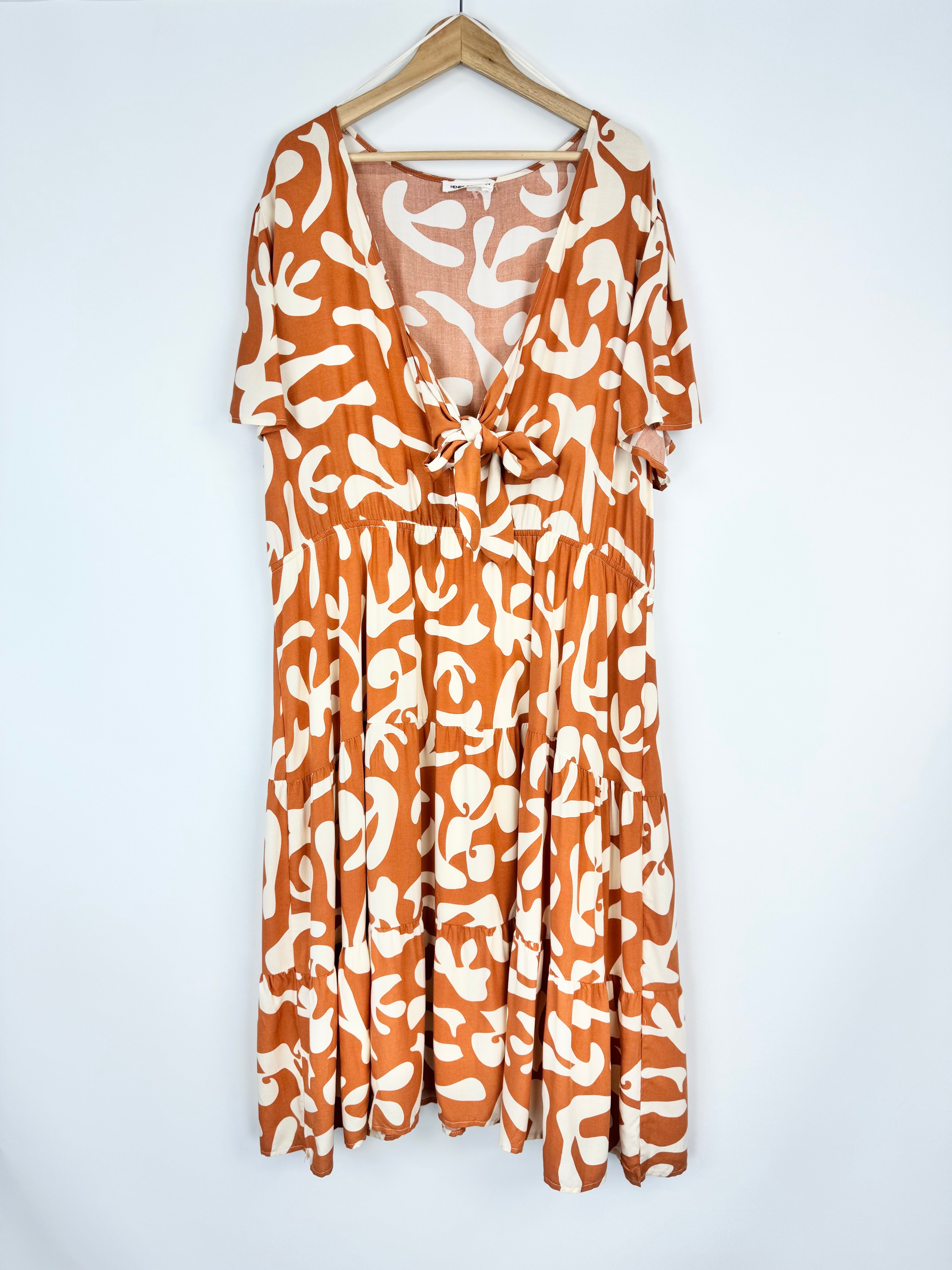Orange and white patterned dress on a hanger against a white background