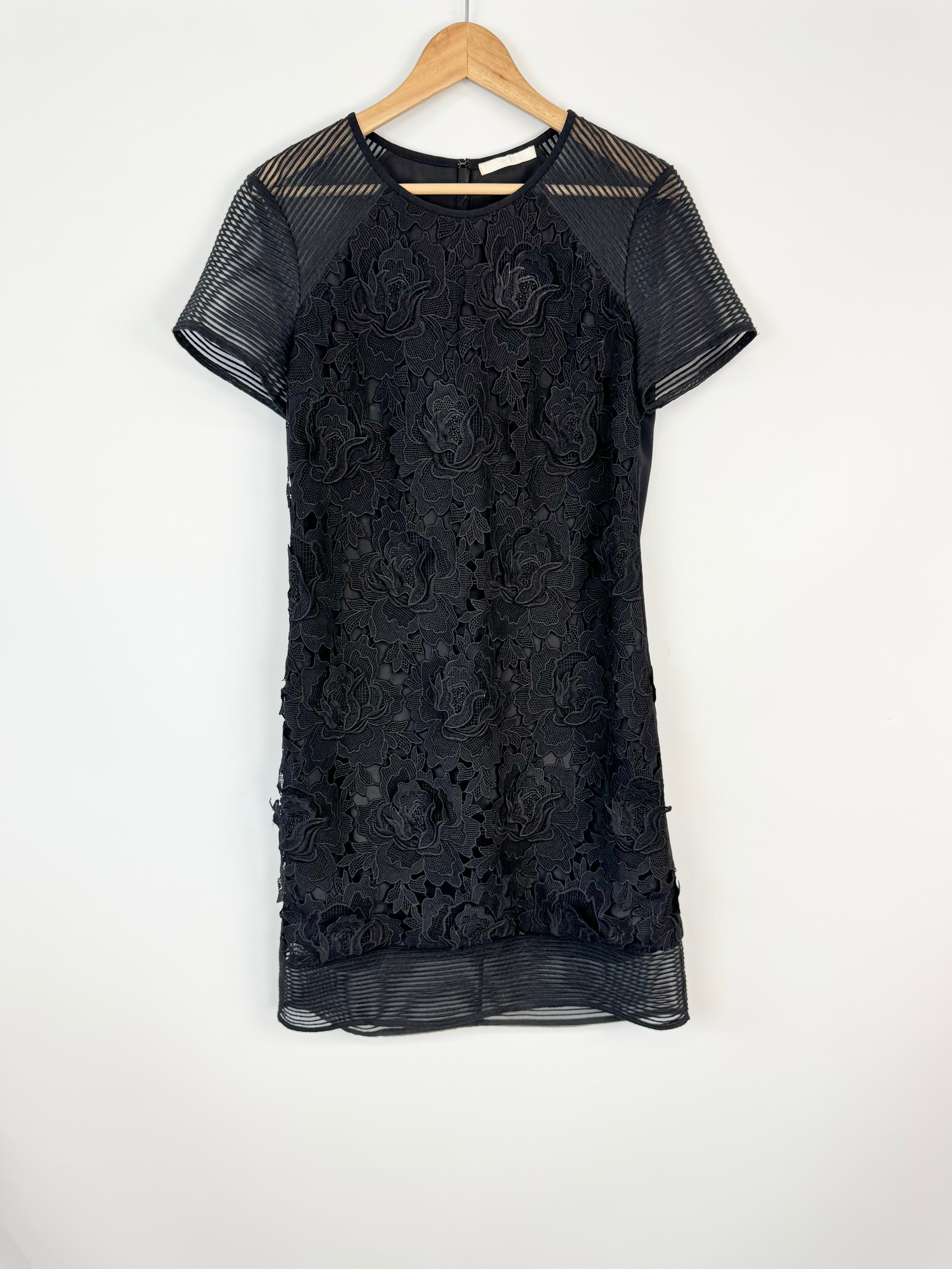Black lace dress on a wooden hanger against a white background