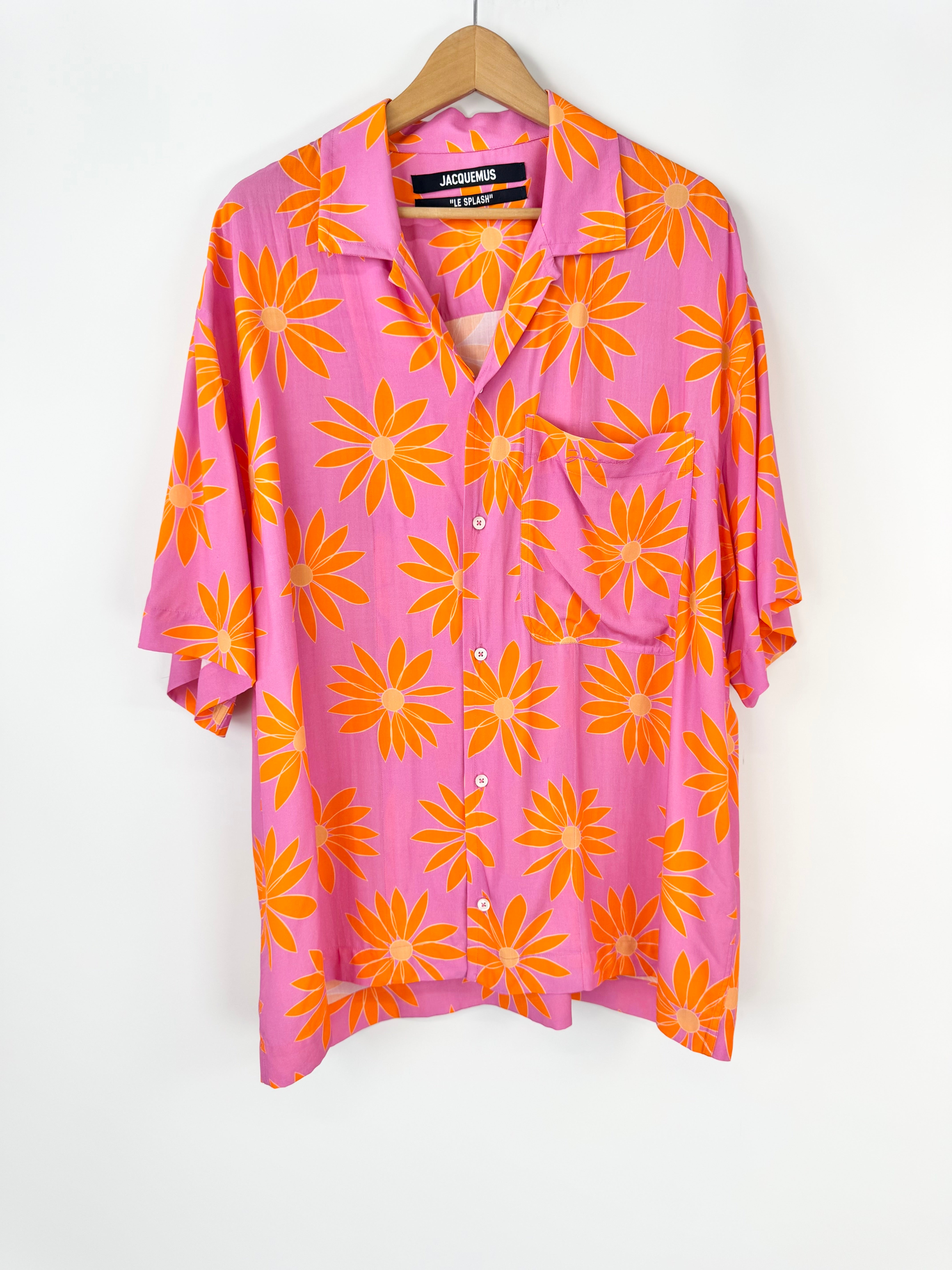 Pink shirt with orange floral pattern on a hanger against a white background