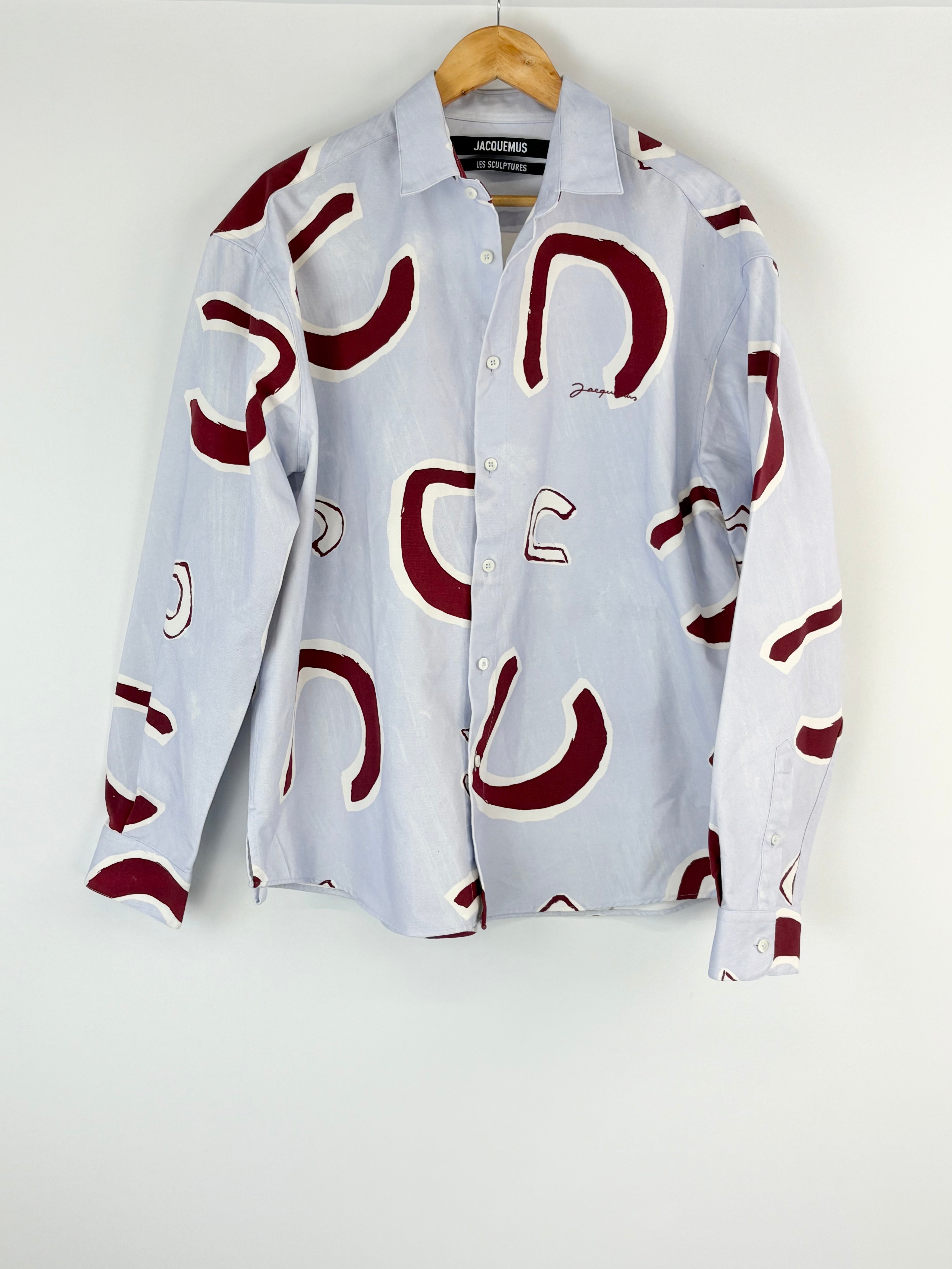 White shirt with red horseshoe pattern on a hanger against a white background