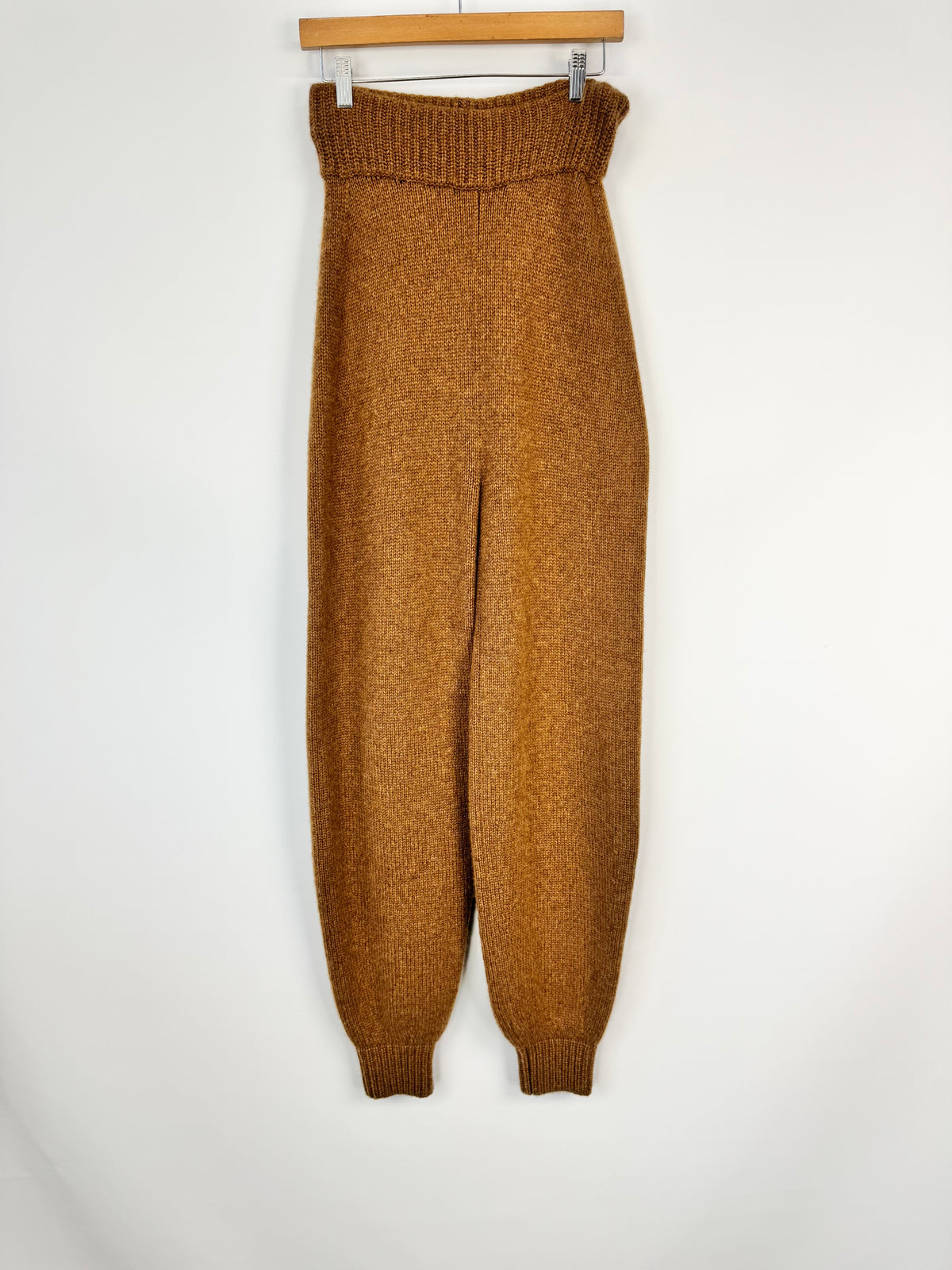 Brown knitted pants hanging on a wooden hanger against a white background