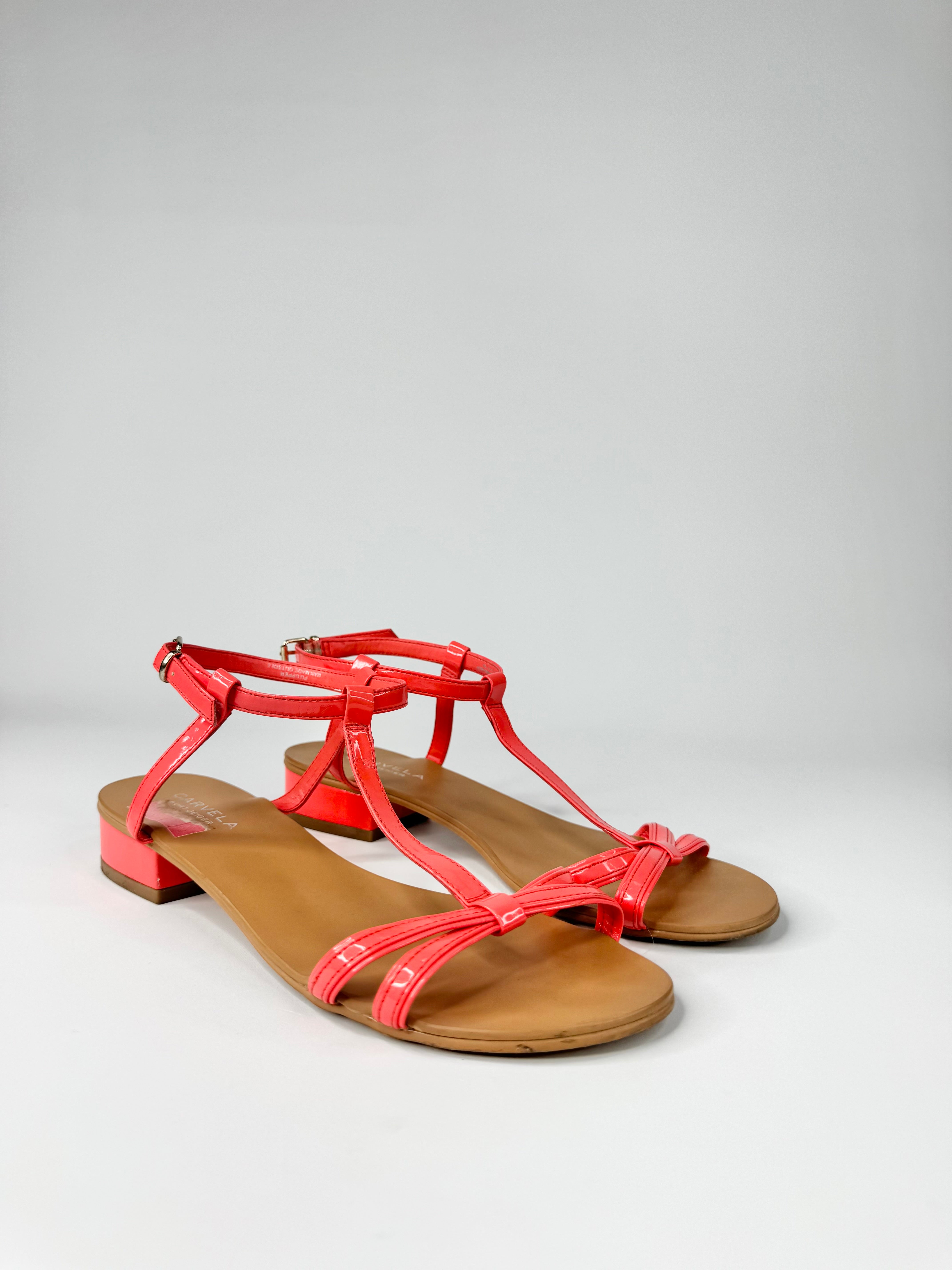 Pair of coral sandals with brown soles on a light gray background