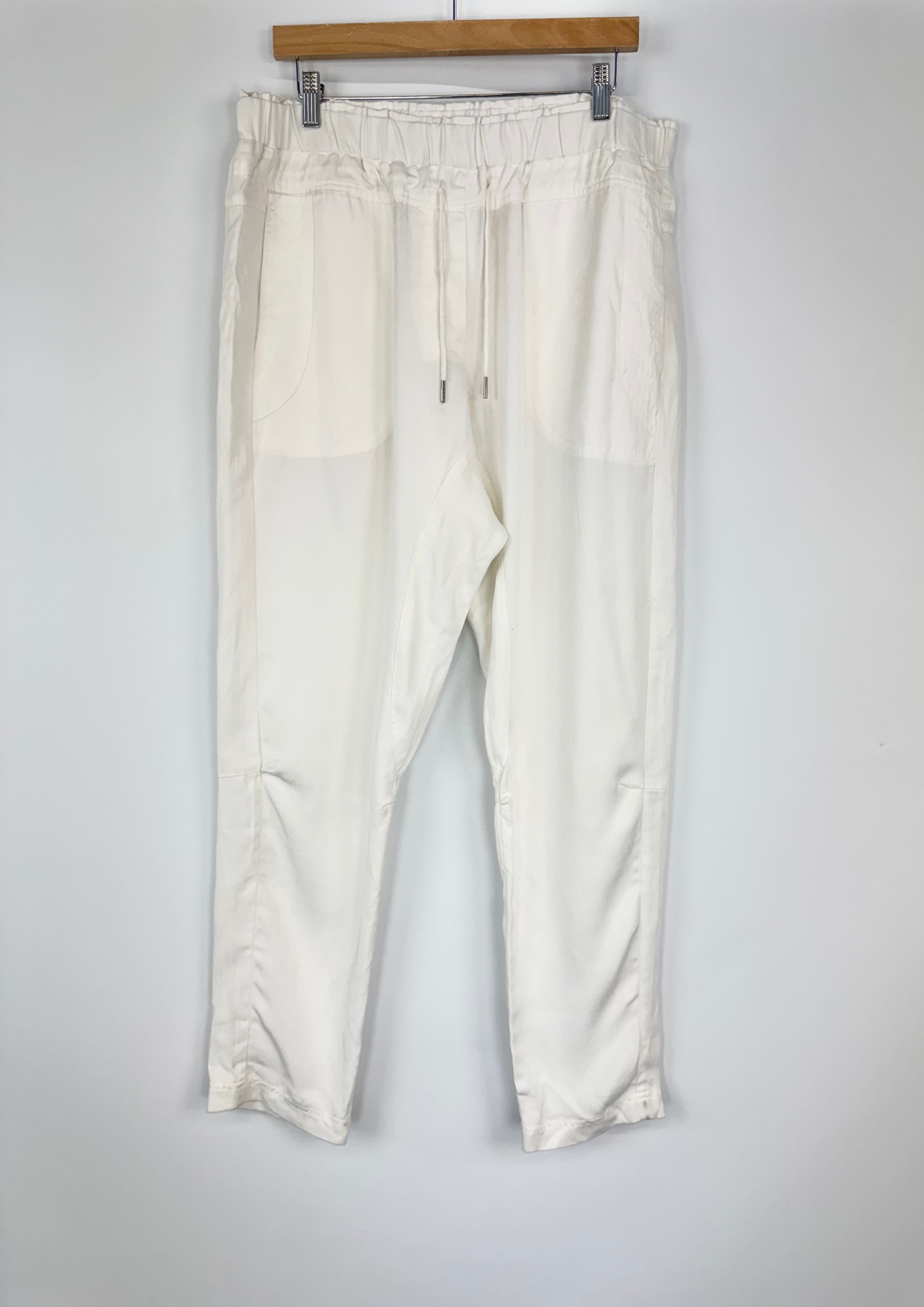 White pants hanging on a wooden hanger against a white background