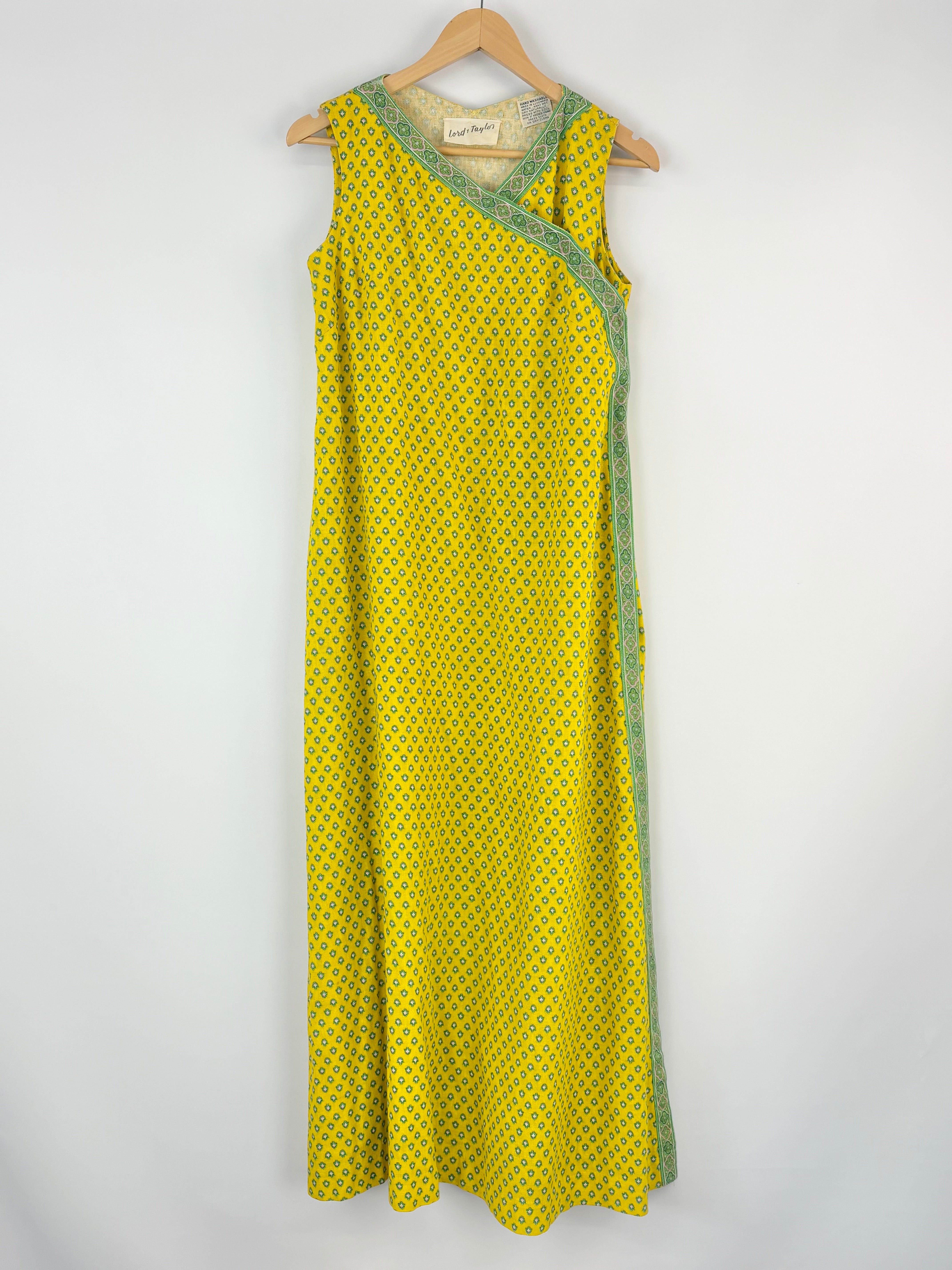 Yellow dress with green trim on a hanger against a white background
