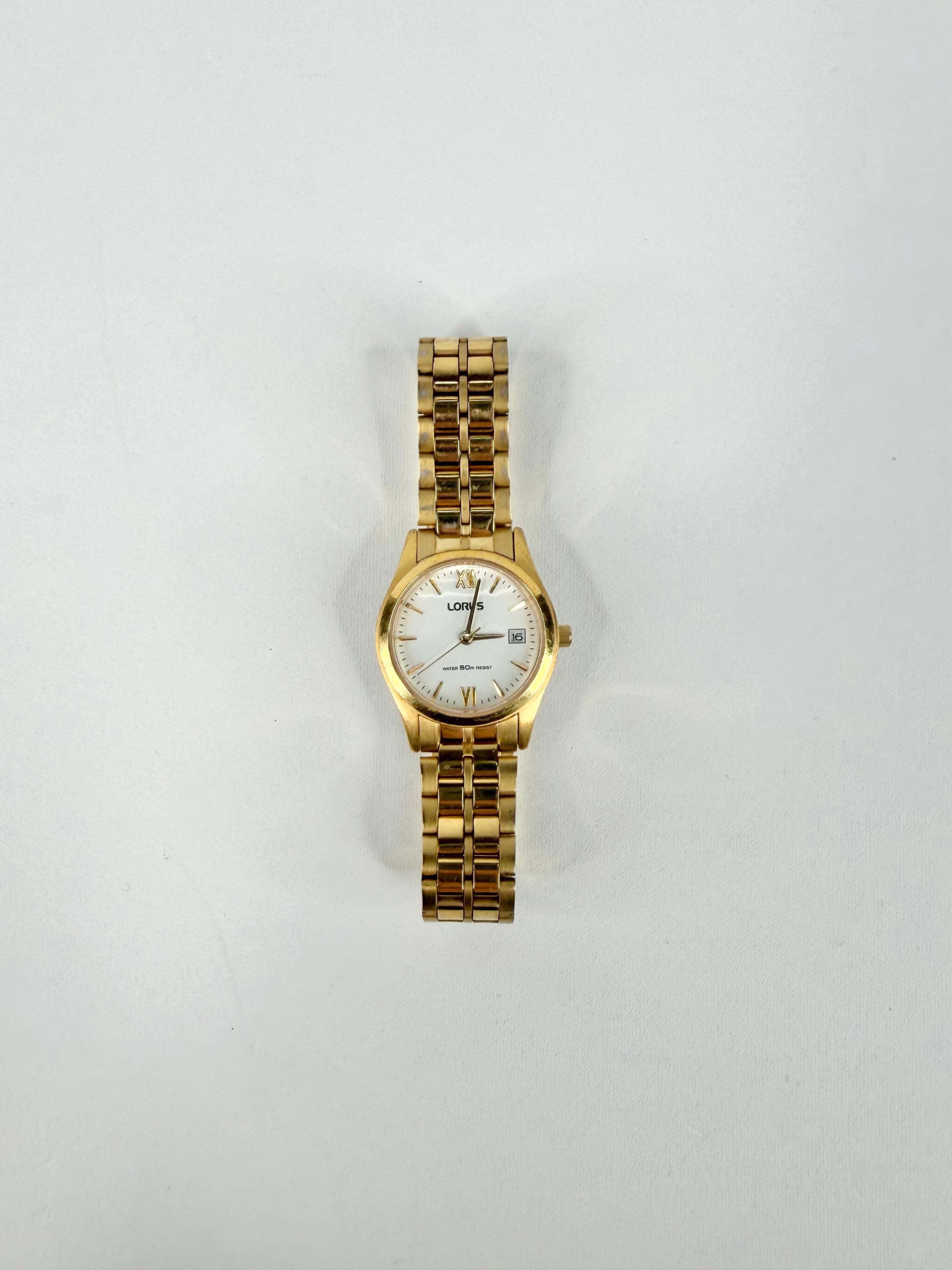 Gold wristwatch with a white face on a light gray background