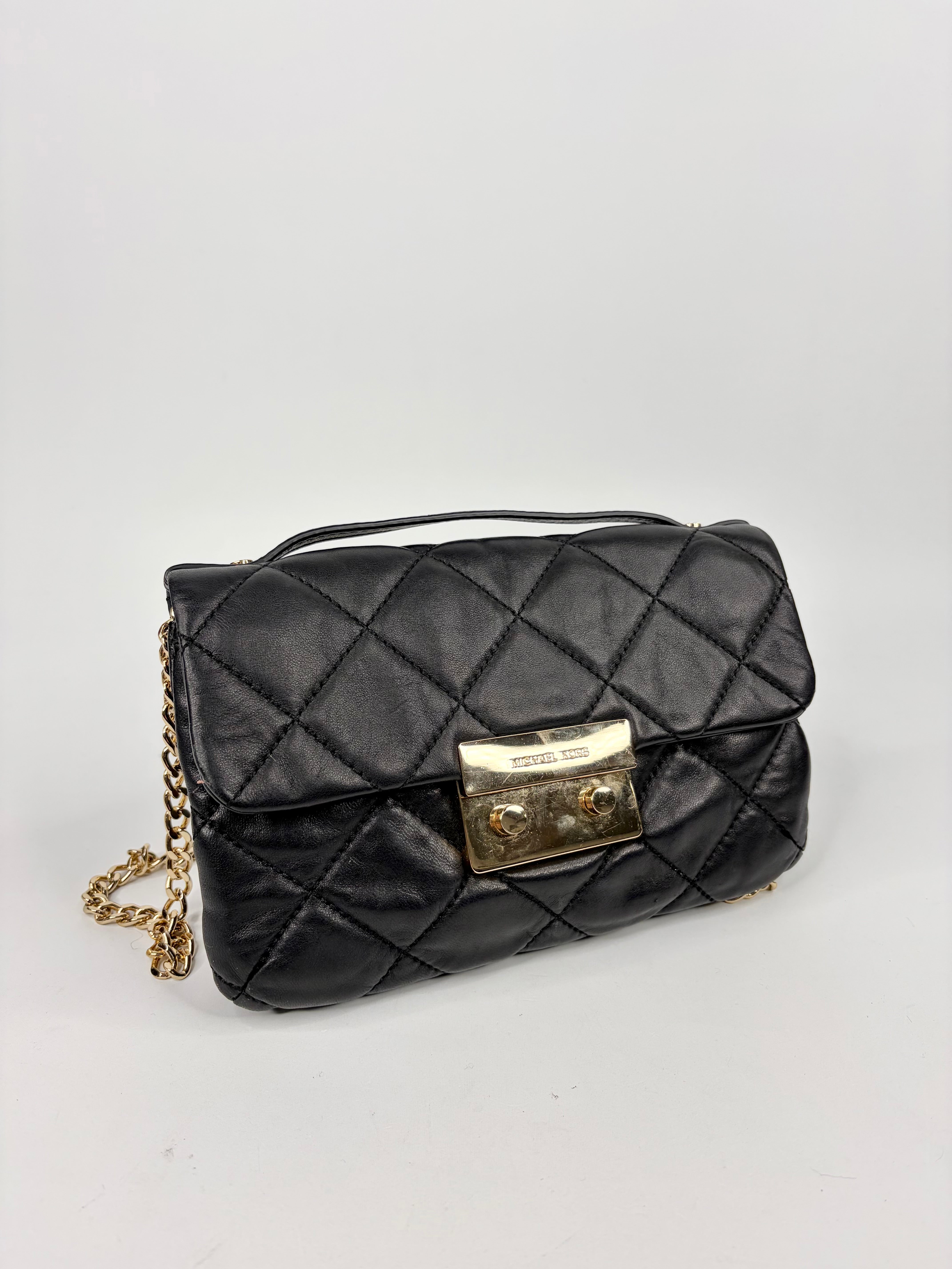 Black quilted handbag with a gold chain and clasp on a light gray background