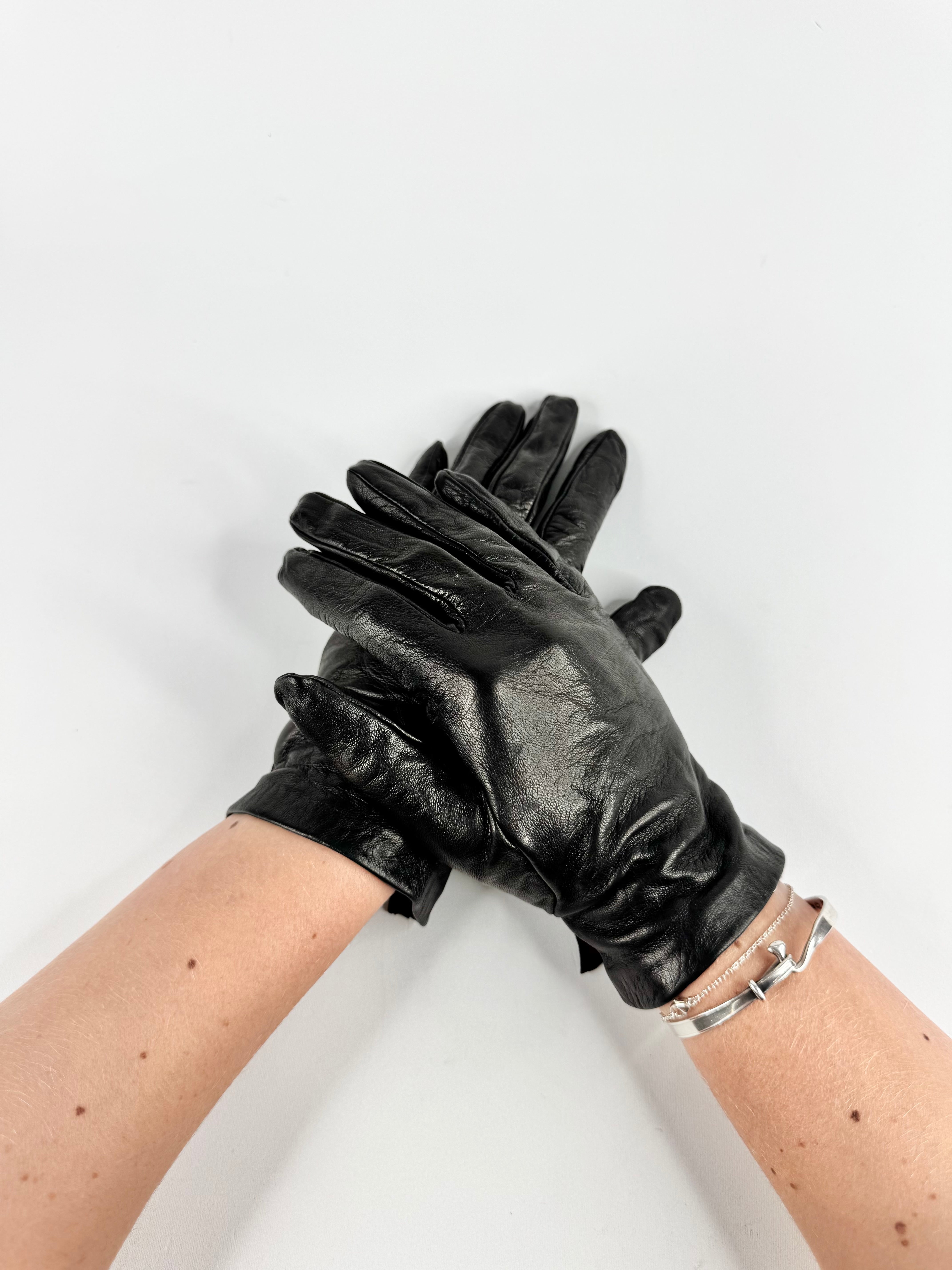 Black leather gloves being worn on a white background