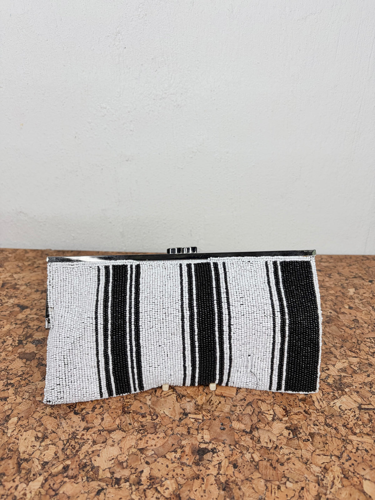 A rectangular beaded clutch bag with vertical black and white stripes, resting on a cork surface against a plain white wall.